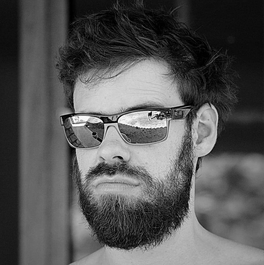 黑白風格 Oakley 太陽眼鏡冒險風情 壁紙 — 一個鬍鬚男嘅黑白肖像，戴住太陽眼鏡，鏡片反射出風景戶外景色。