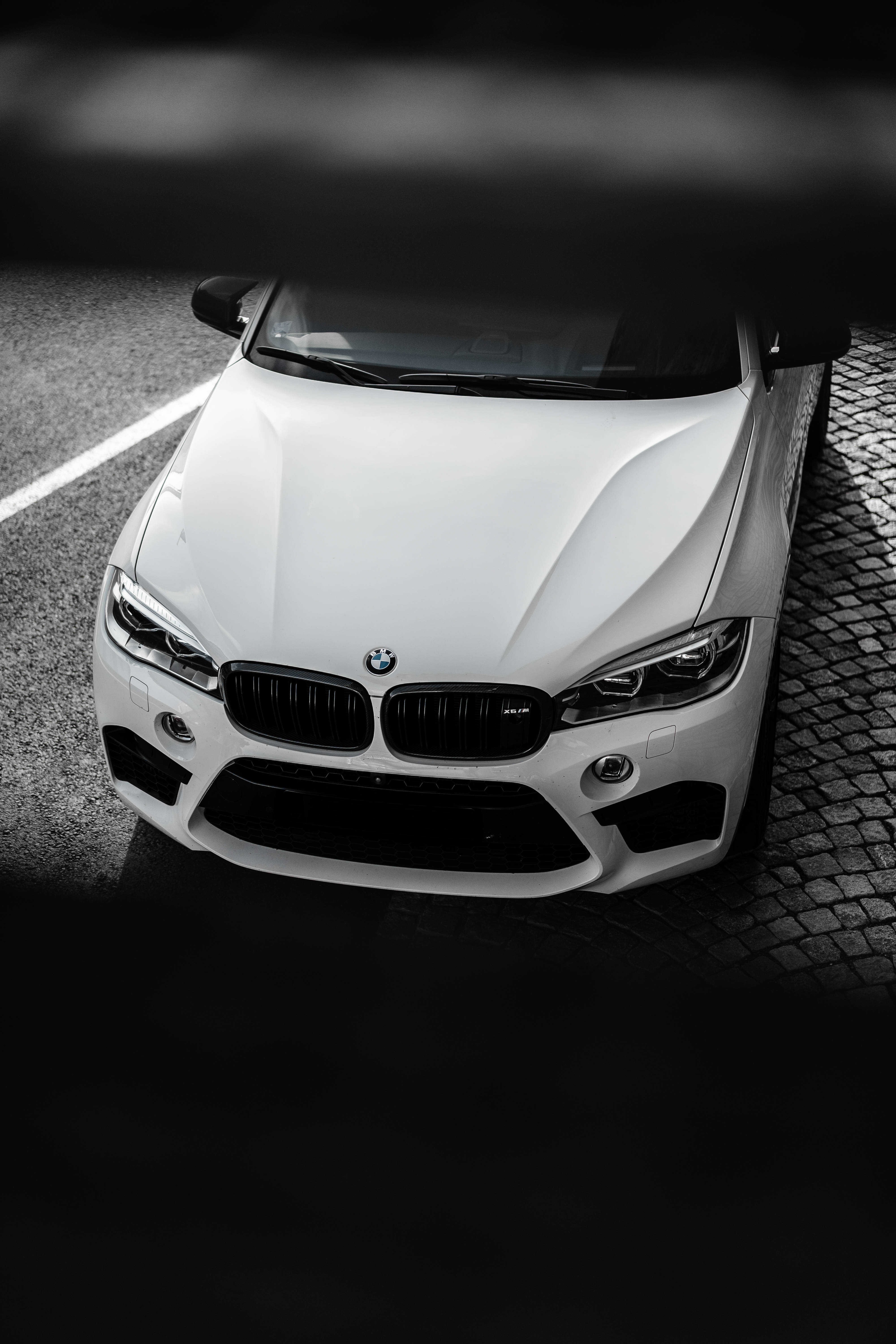 黑白高清BMW汽車 壁紙 — 一輛時尚的白色BMW跑車停泊在鵝卵石街道上，在戲劇性的高對比度燈光下。