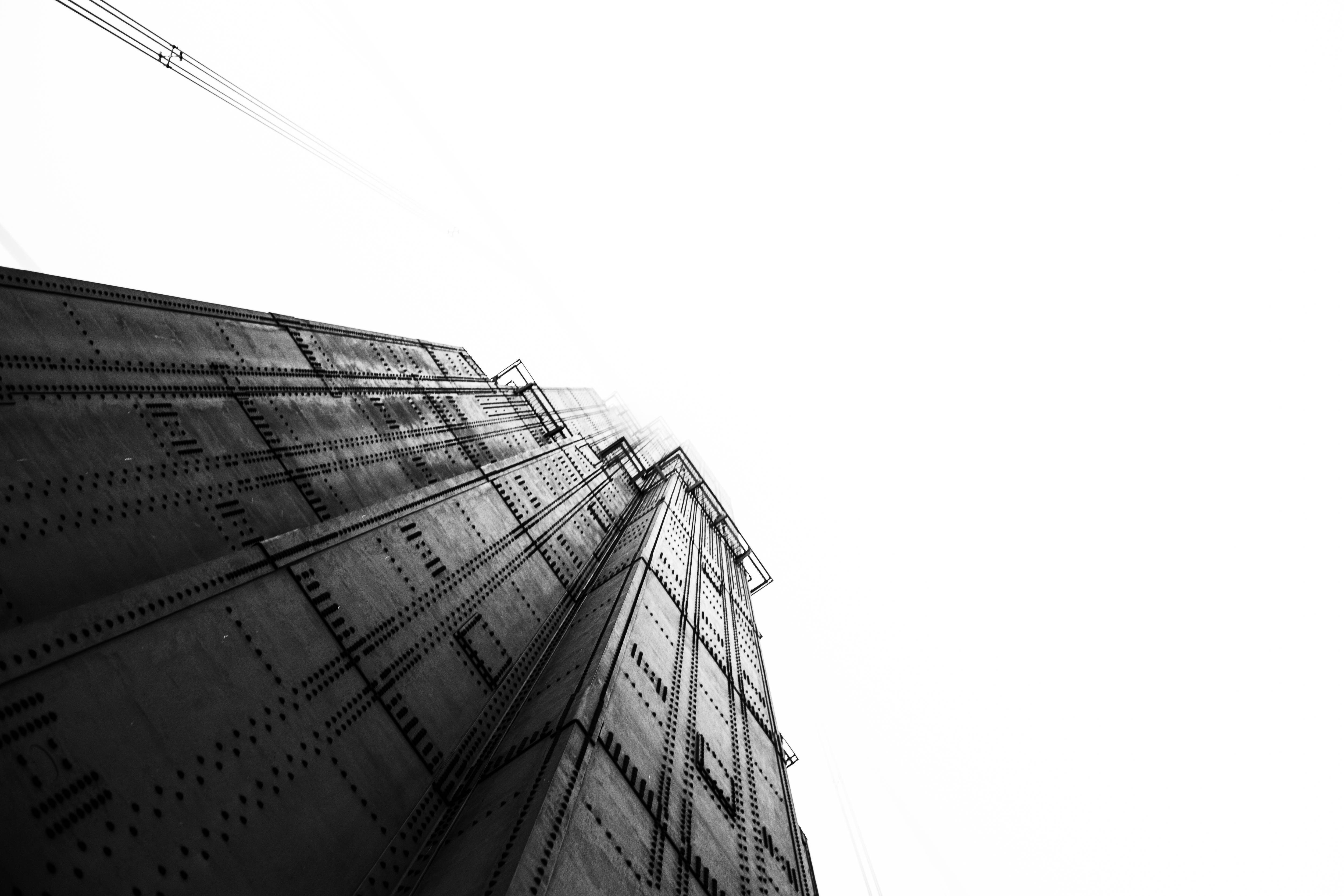 黑白高清建築 壁紙 — 一張清晰的黑白低角度照片，拍攝了一座高聳的工業鋼結構建築刺穿明亮的天空。