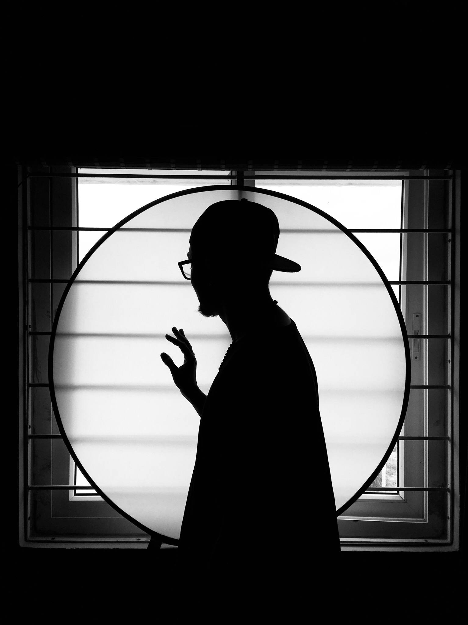 黑白高畫質男子剪影 壁紙 — 一個戴帽子和眼鏡的男人的鮮明黑白剪影，被一個圓形窗戶框住，背景明亮。