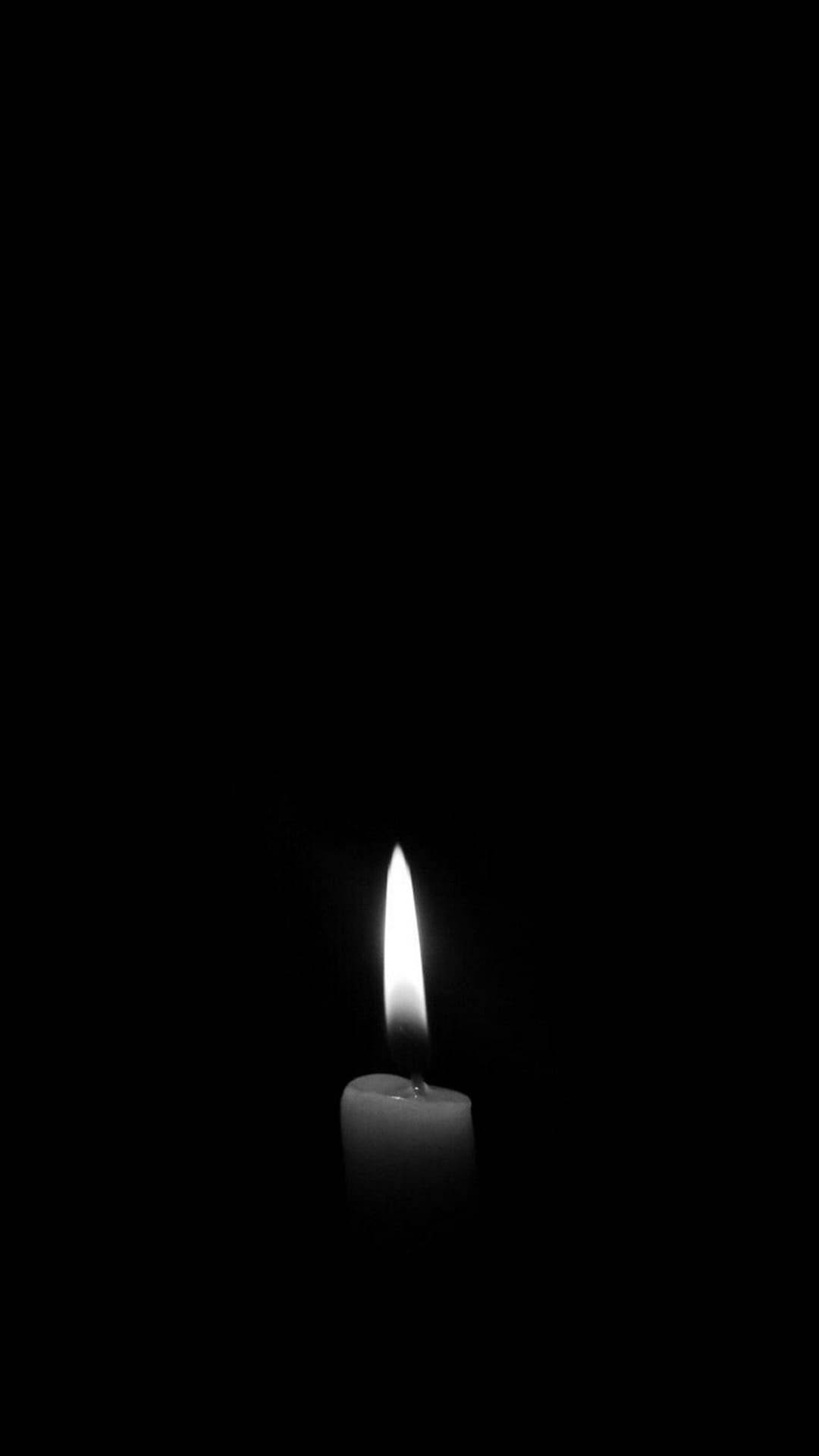 黑白點燃蠟燭極簡暗黑 iPhone 壁紙 — 一支點燃的蠟燭在漆黑背景上投射出柔和的光芒，構成極簡的黑白構圖。