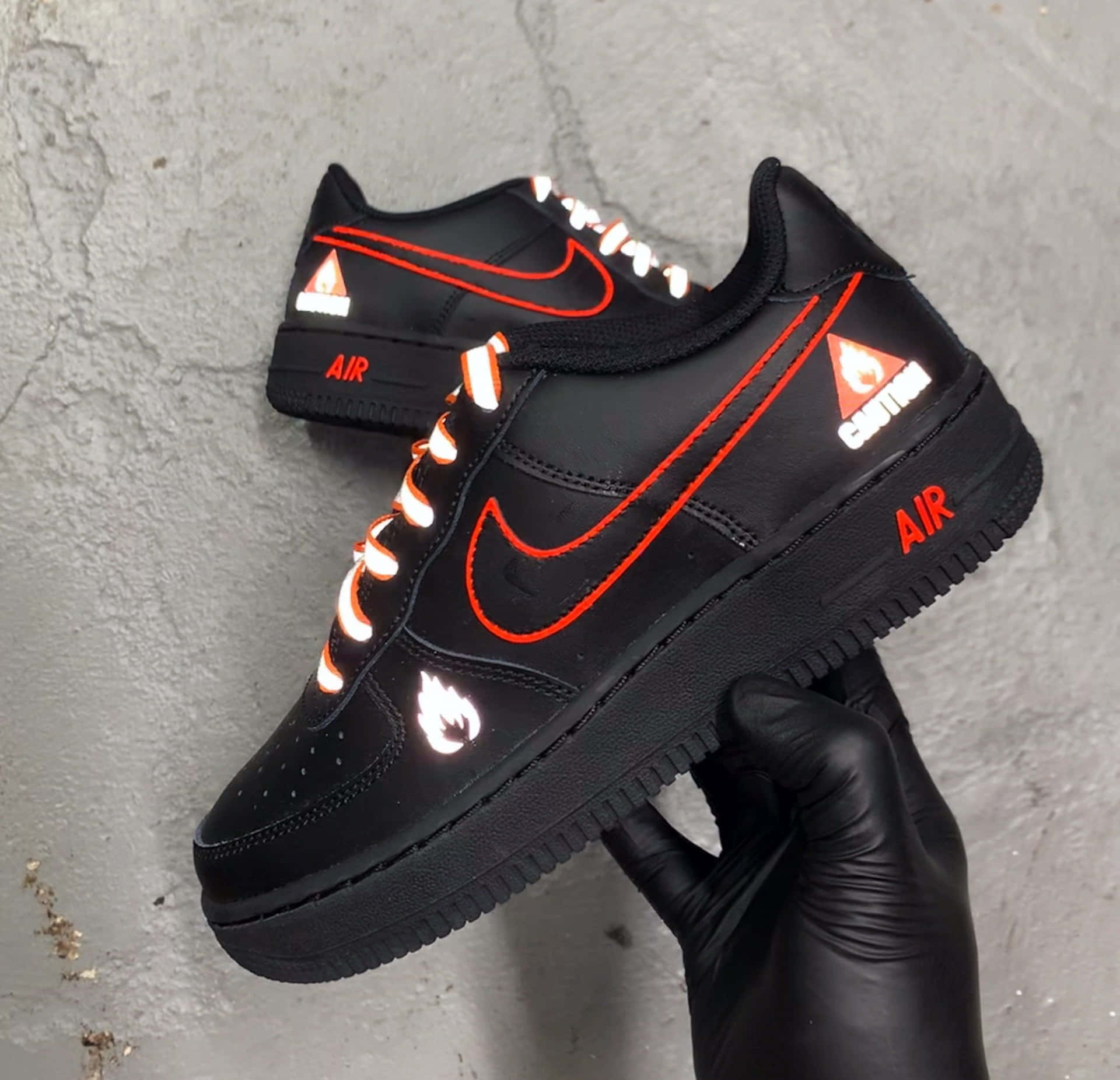 戴手套的手拿著一對黑色Nike運動鞋，帶有發光的橙色和白色細節。