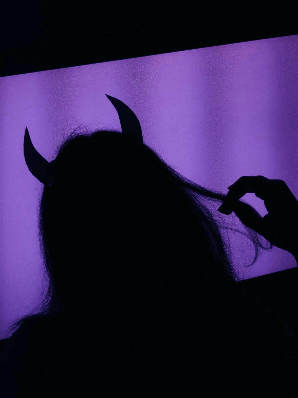 黑紫風格魔鬼風 壁紙 — 一個帶有惡魔角的人影，在發光的紫色背景下輕輕觸摸頭髮的剪影。