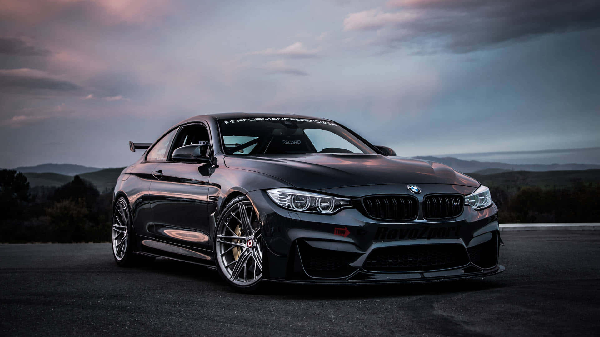 黑色 2016 BMW M4 GTS 1920x1080 M系列背景 壁紙 — 一輛時尚的黑色BMW M4雙門轎跑車，配備定制輪圈和後擾流板，在黃昏時分停在瀝青路上，背景是起伏的山丘。
