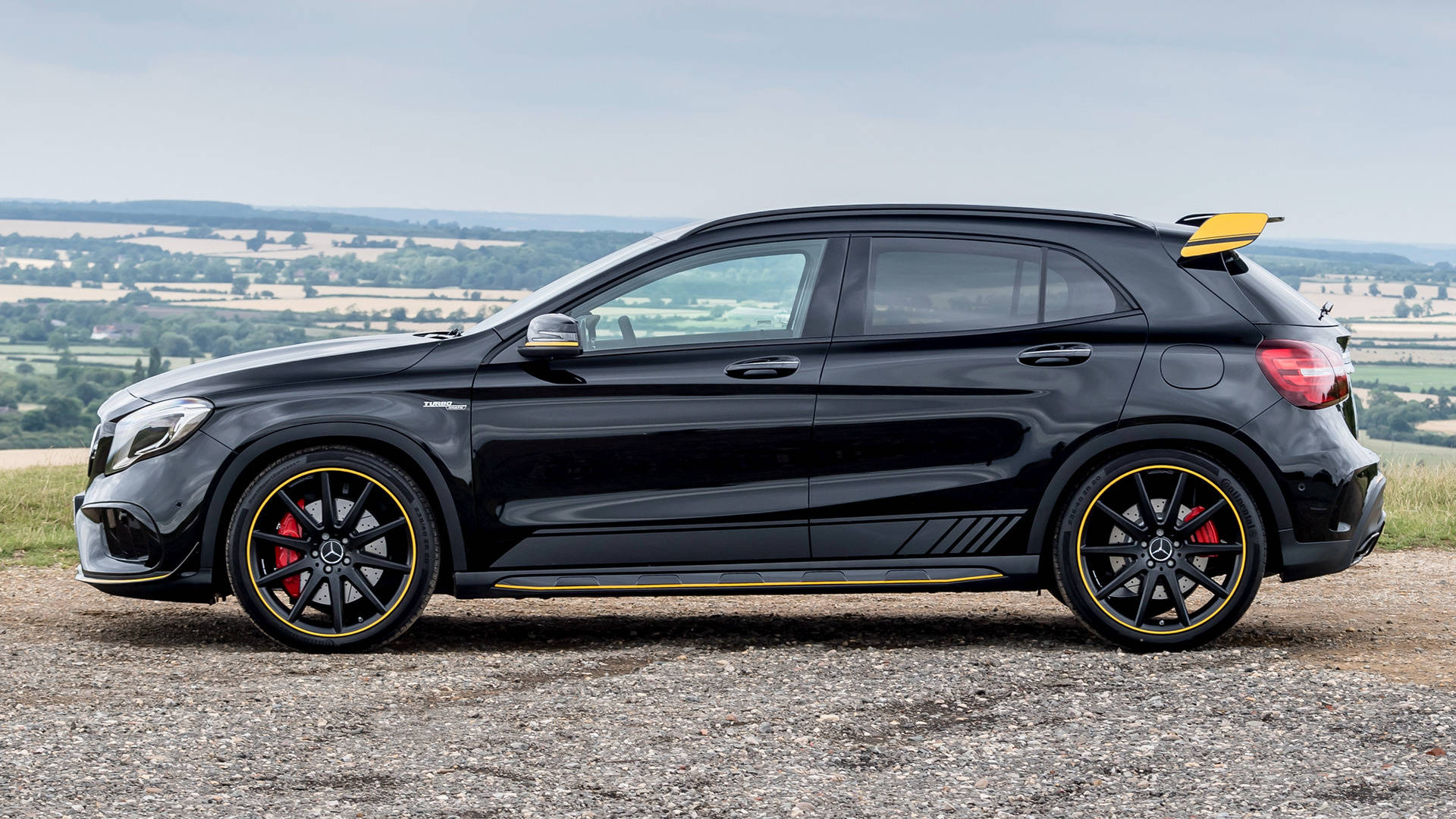 黑色Mercedes-AMG GLA45 S SUV帶有黃色點綴，停在碎石上俯瞰鄉村。