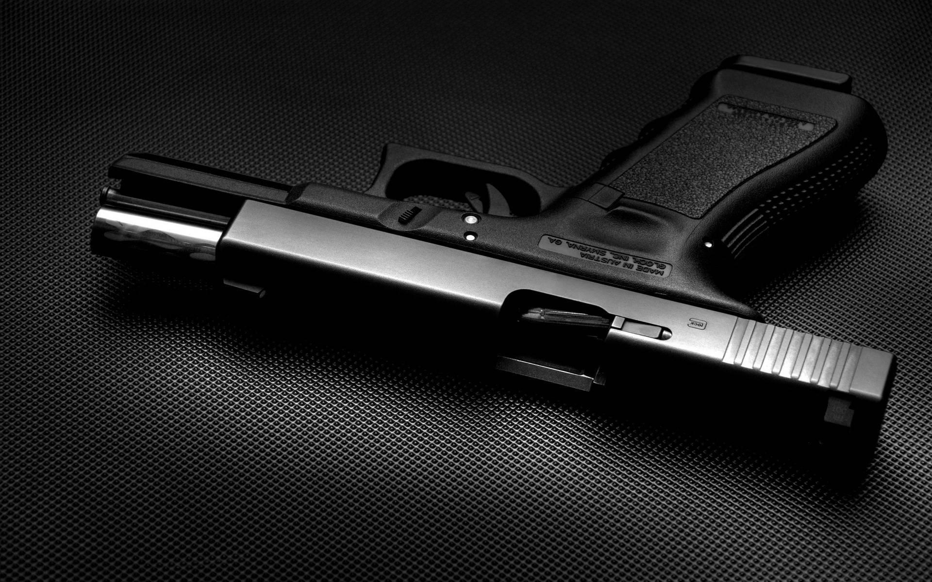 黑色 Glock 滑套開啟 壁紙 — 一把時尚的黑色手槍在戲劇性的工作室燈光下斜放在有紋理的深色表面上。
