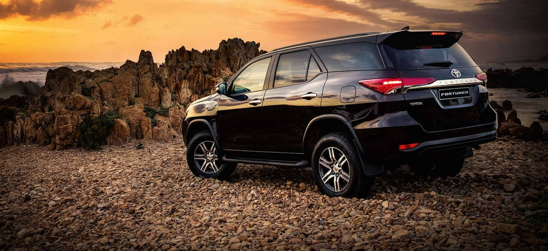 日落時分黑色豐田 Fortuner SUV 停泊在岩石海灘上