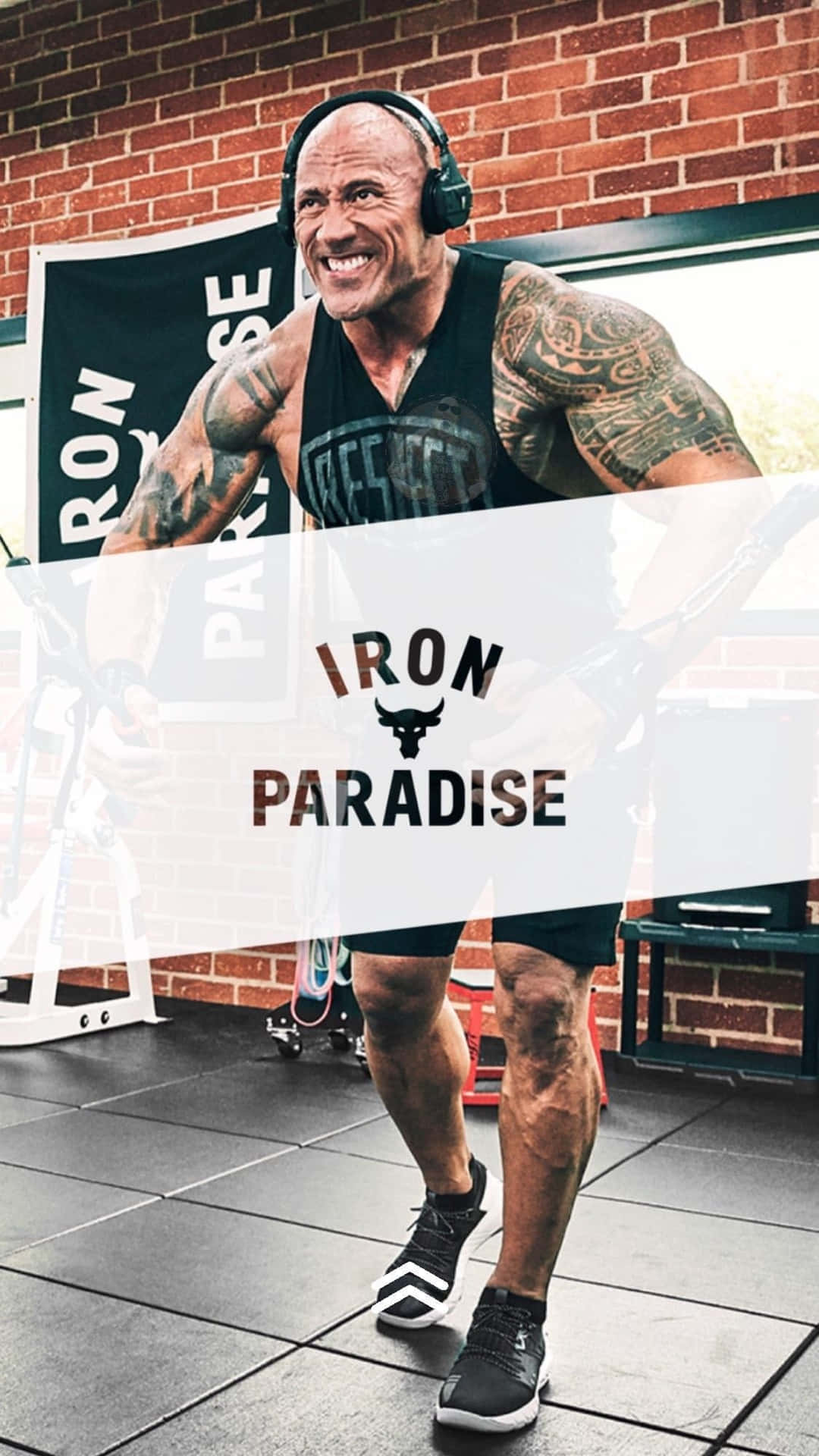 Dwayne Johnson 喺健身房戴住耳機微笑舉重。