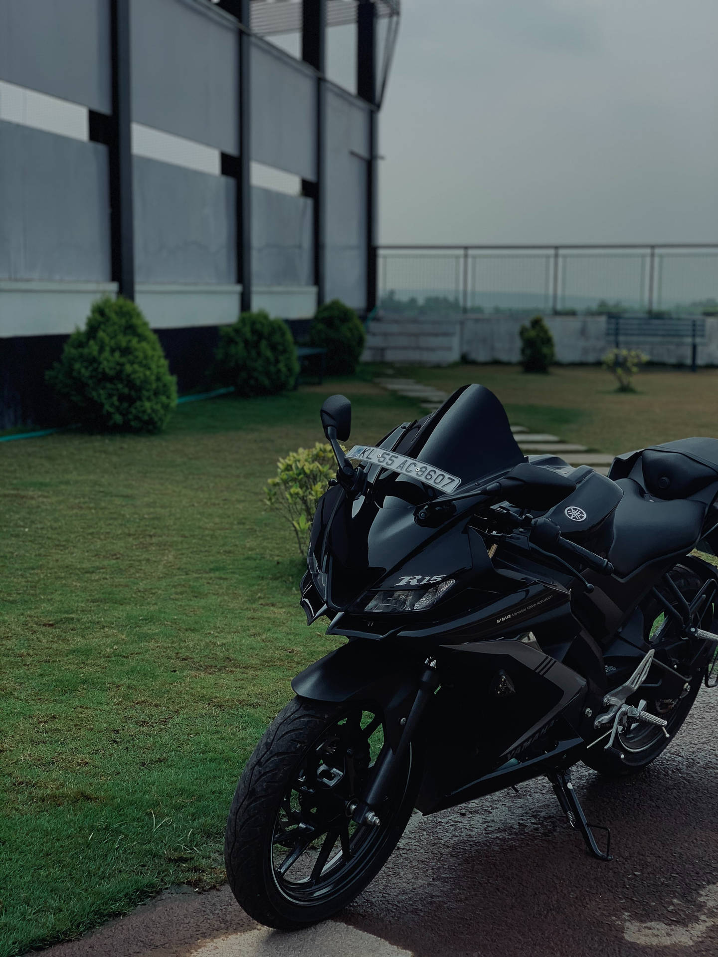 啞光黑色Yamaha R15電單車停泊在濕漉漉的行人路上，靠近現代建築物和綠色灌木。