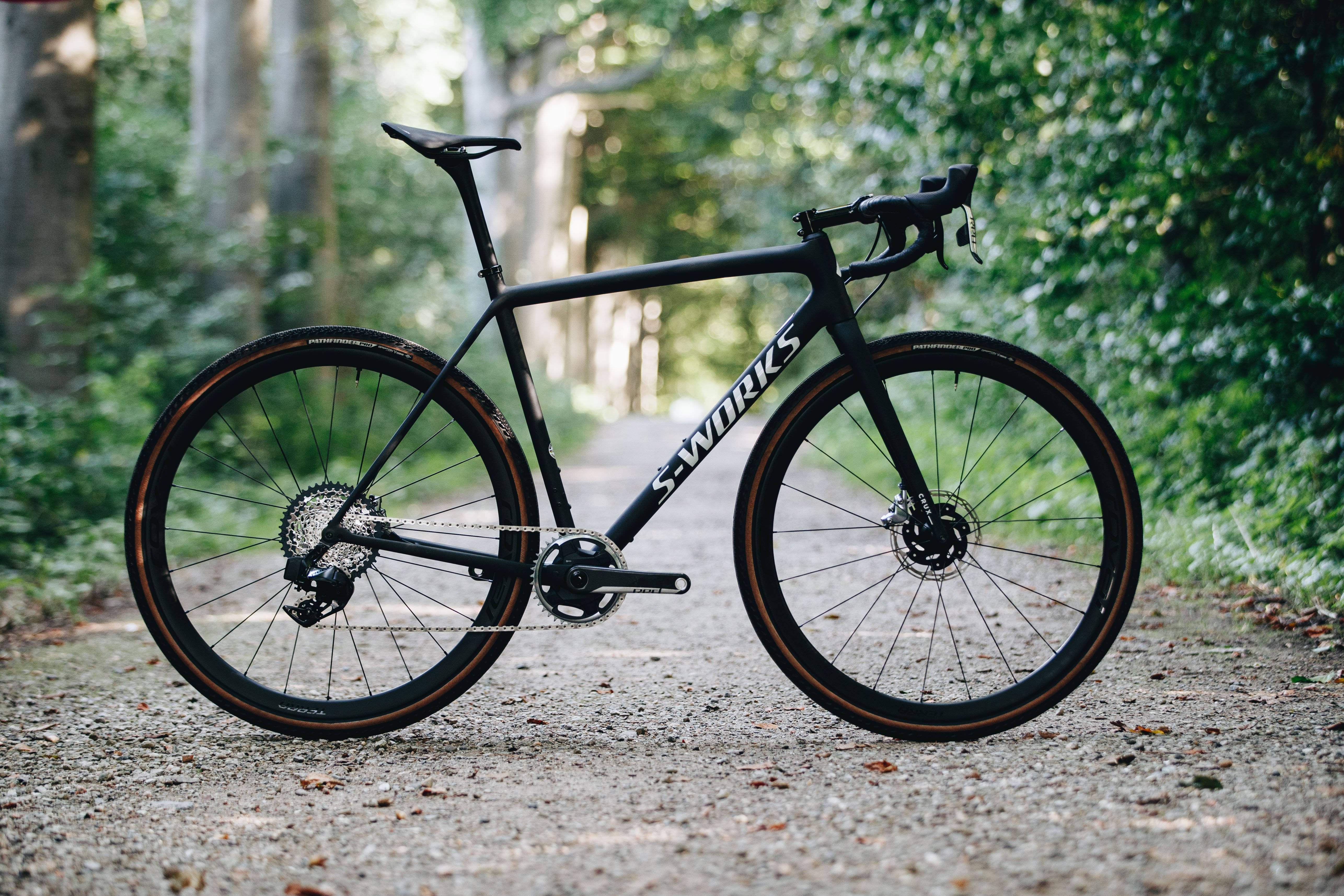 黑色 Specialized 自行車戶外 壁紙 — 一輛時尚的黑色S-Works公路單車配橙色輪胎，停放在綠樹成蔭的森林碎石小徑上。