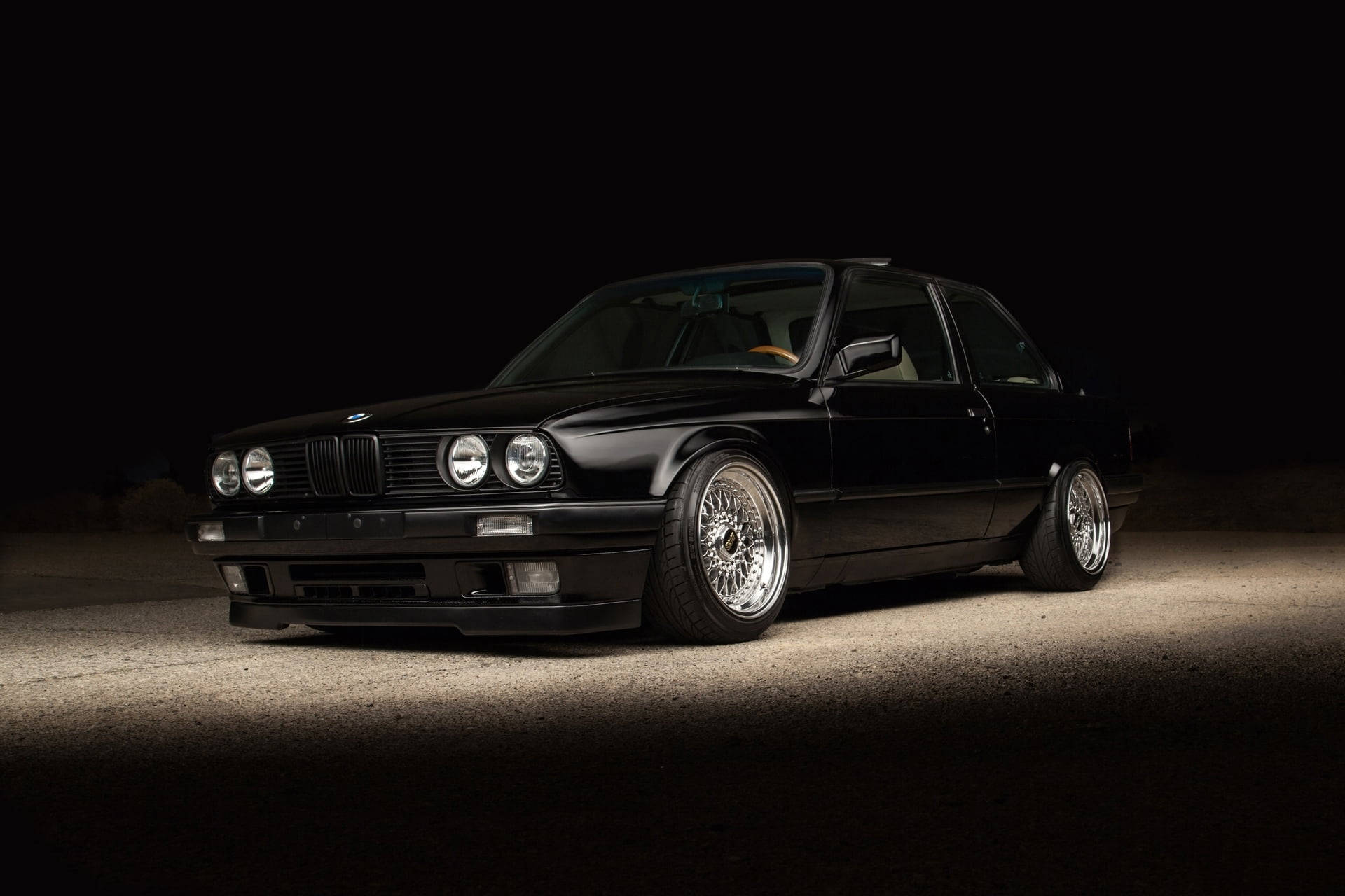 黑色BMW E30雙門轎跑車配備定制輪圈，在夜間沙漠環境中照亮。