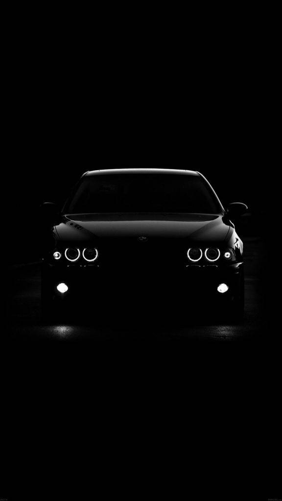 黑色BMW肖像預覽 壁紙 — 一輛時尚汽車的發光車頭燈在極簡黑白照片中刺穿黑暗。