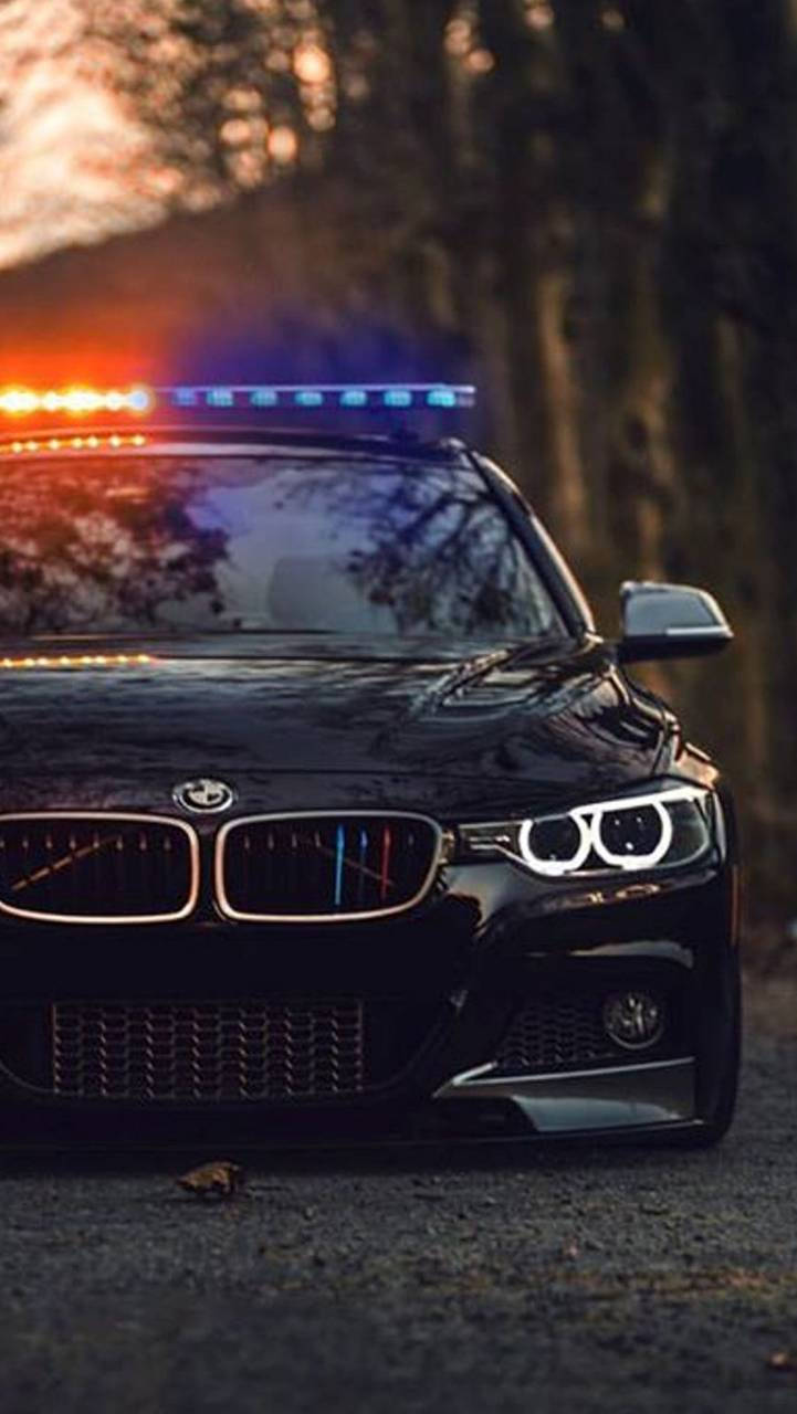 黃昏時停泊在樹林地區的黑色警車，帶有閃爍燈光。