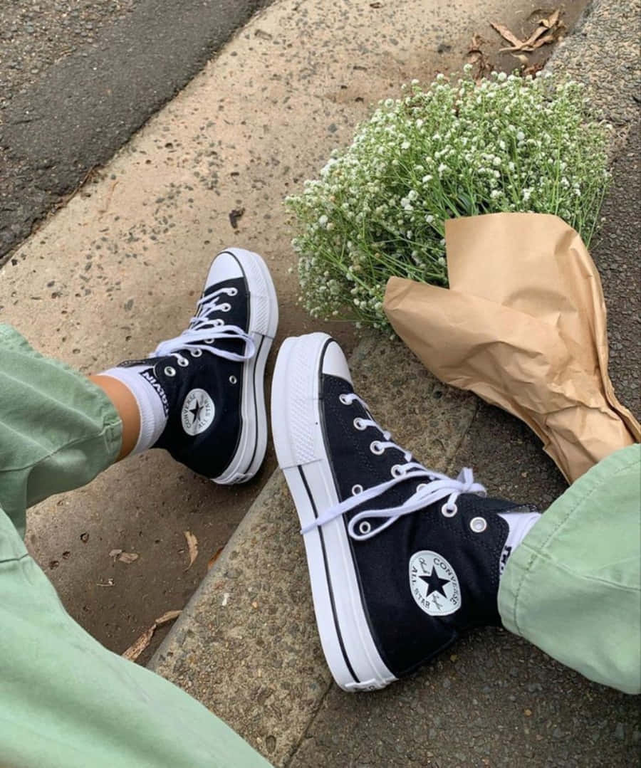 鞋子 桌布 壁紙 — 黑色Converse運動鞋配白色鞋帶，旁邊放著一束用紙包裹的滿天星花束，放在行人路上。