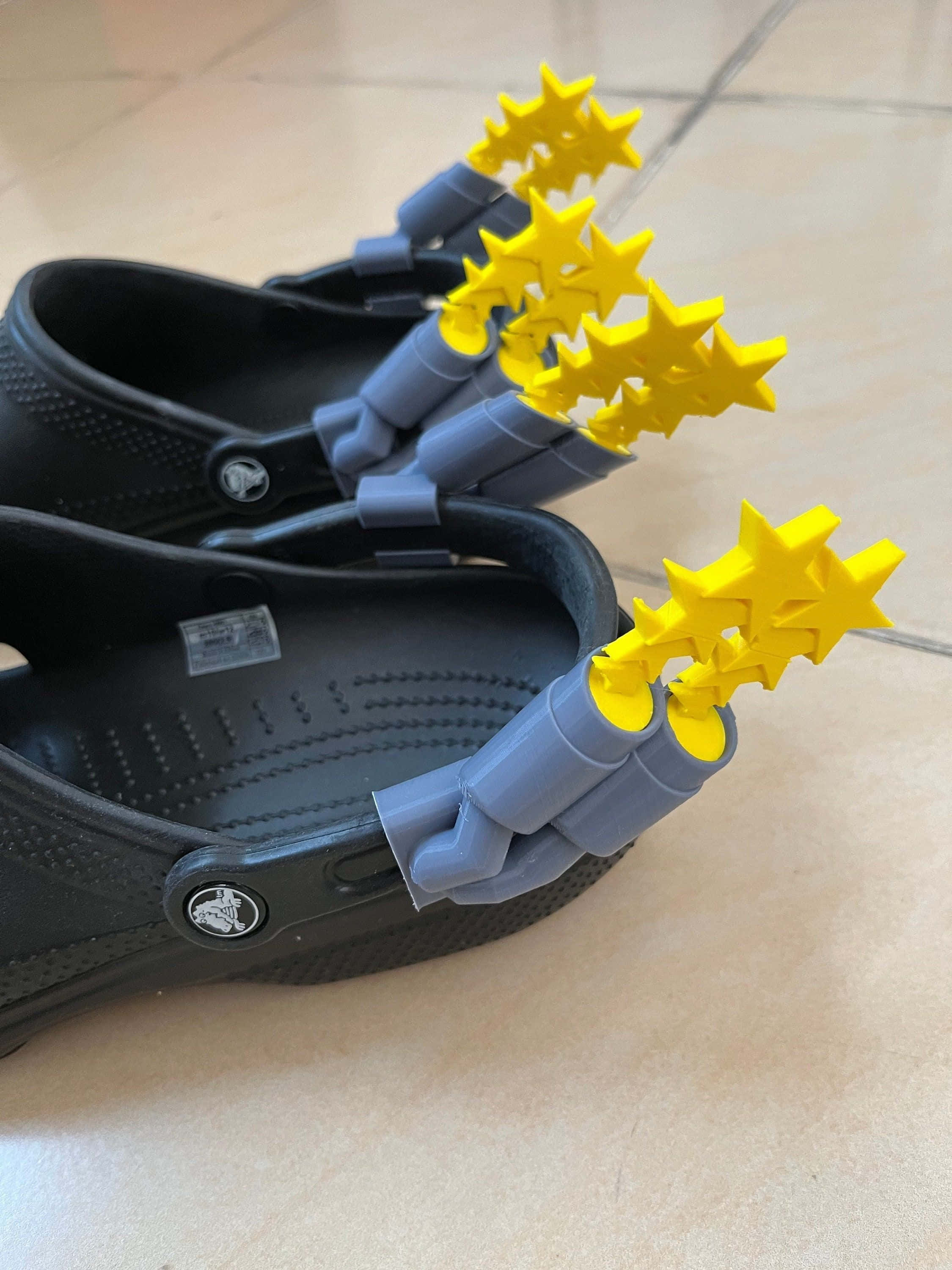 Sandals 桌布 壁紙 — 黑色Crocs鞋，鞋帶上附有亮黃色星形釘，置於瓷磚地板上。