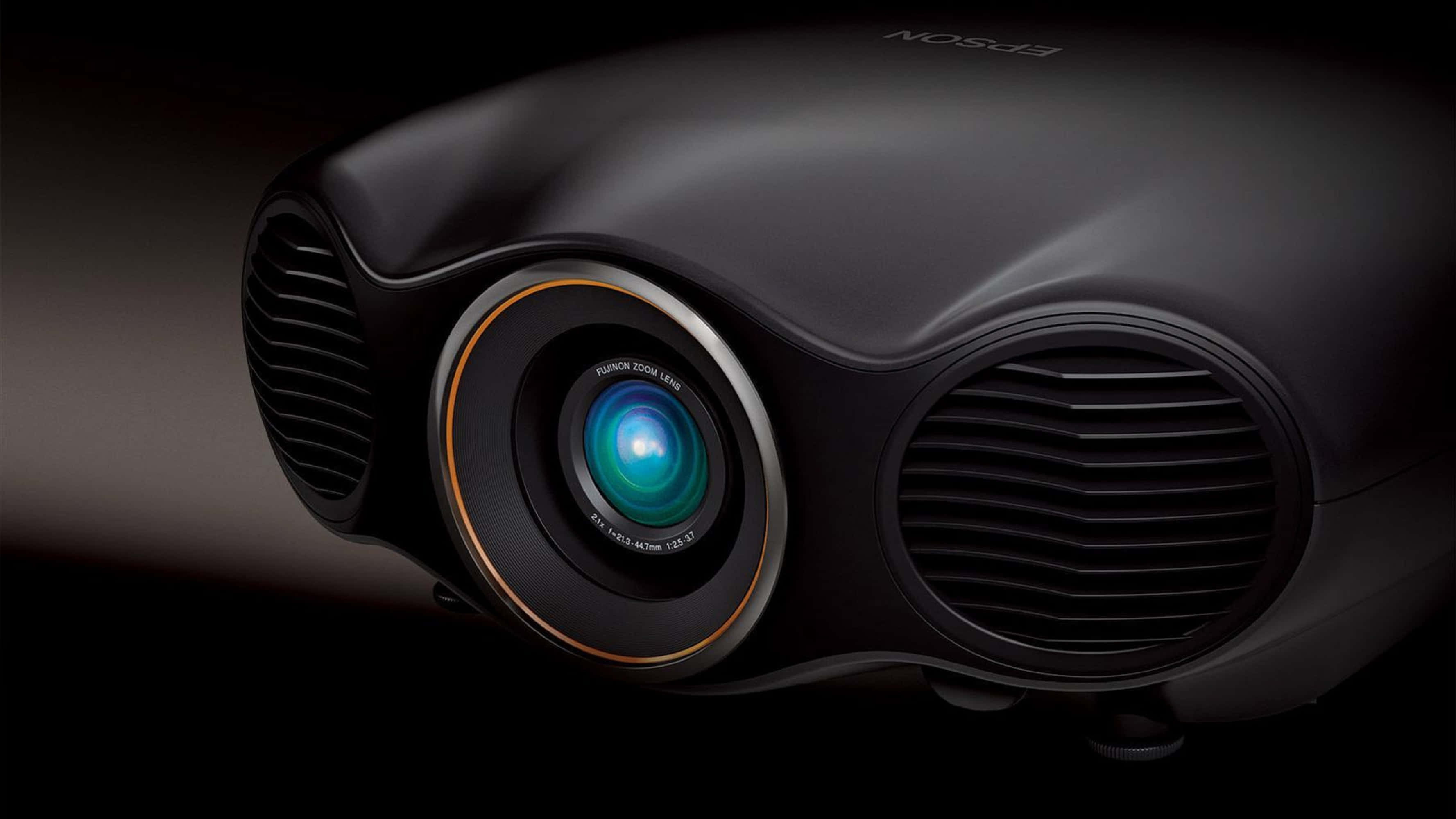 4K Projector 桌布 壁紙 — 黑色Epson投影機特寫，帶有發光藍色鏡頭，背景昏暗。