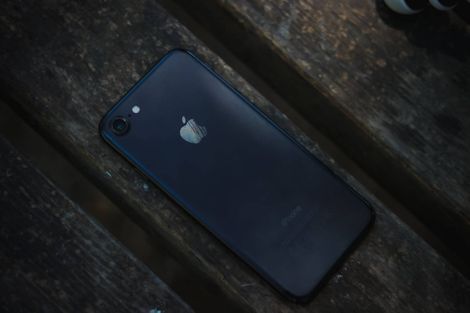 黑色iPhone 7置於木質表面 壁紙 — 深藍色iPhone 7在昏暗燈光下擱在風化的木板上。