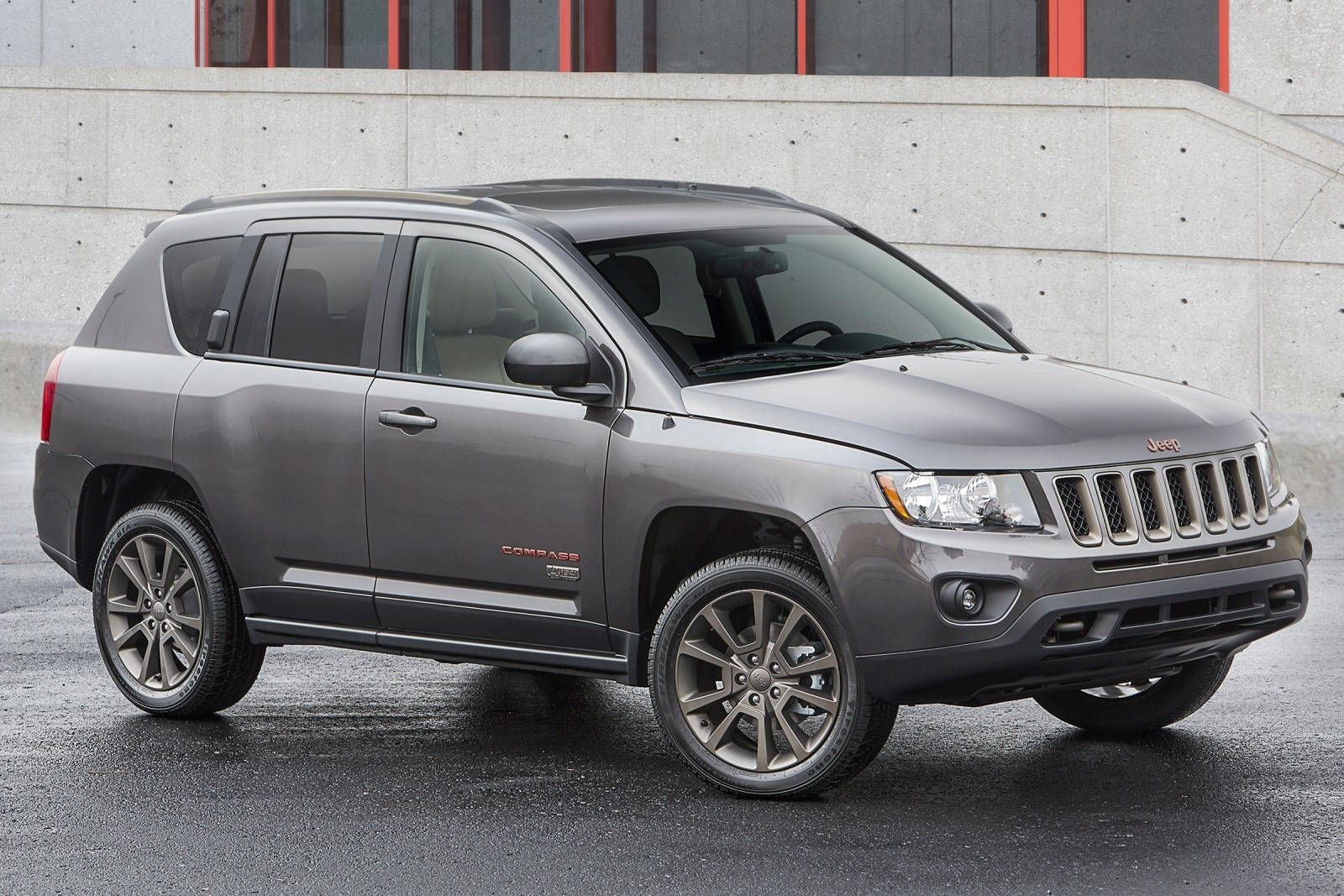 灰色Jeep Compass SUV停泊在濕漉漉的路面上，靠近帶有紅色點綴的混凝土牆。