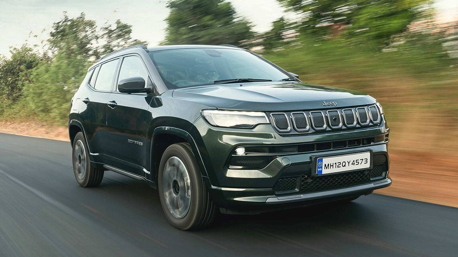深綠色Jeep Compass SUV在道路上行駛，背景有動態模糊效果。