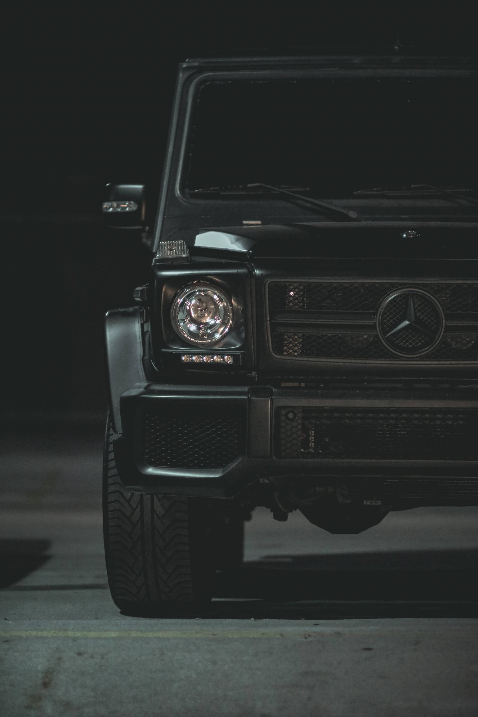 黑色Mercedes豪華越野車 壁紙 — 一部時尚的黑色 Mercedes G-Wagen 在夜間被戲劇性地照亮，其標誌性鬼面罩和圓形頭燈在黑暗的城市背景下發光。