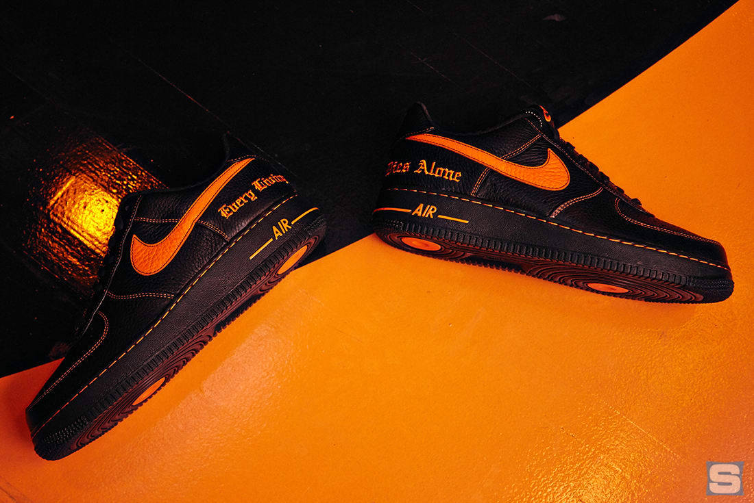 VLONE x Nike Air Force One 壁紙 — 黑色Nike Air Force 1運動鞋帶有鮮明的橙色點綴，斜放在充滿活力的橙色表面上，背景為深色紋理。