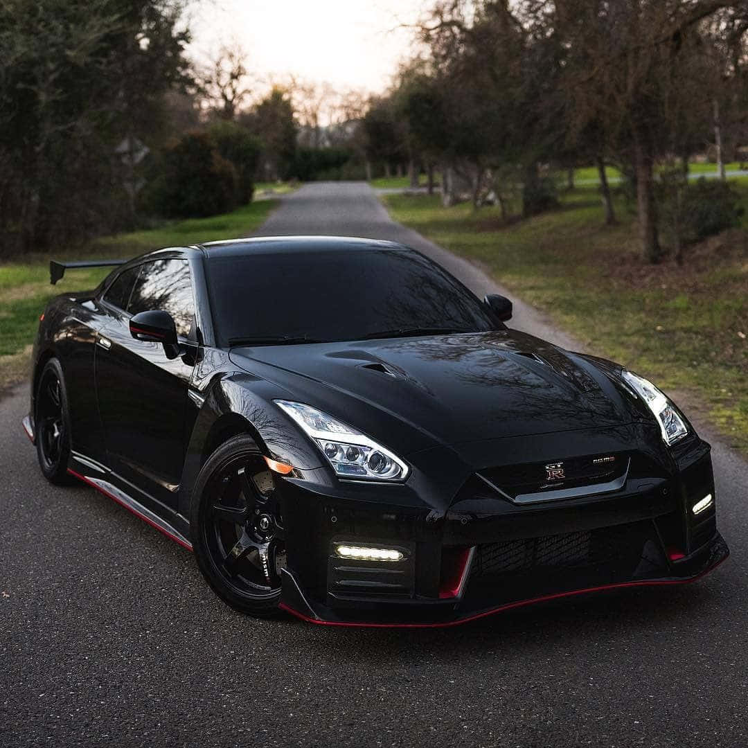 黑色Nissan R35 GT-R圖 壁紙 — 一輛帶有紅色點綴的時尚黑色日產GT-R，在黃昏時停泊在綠樹成蔭的道路上。