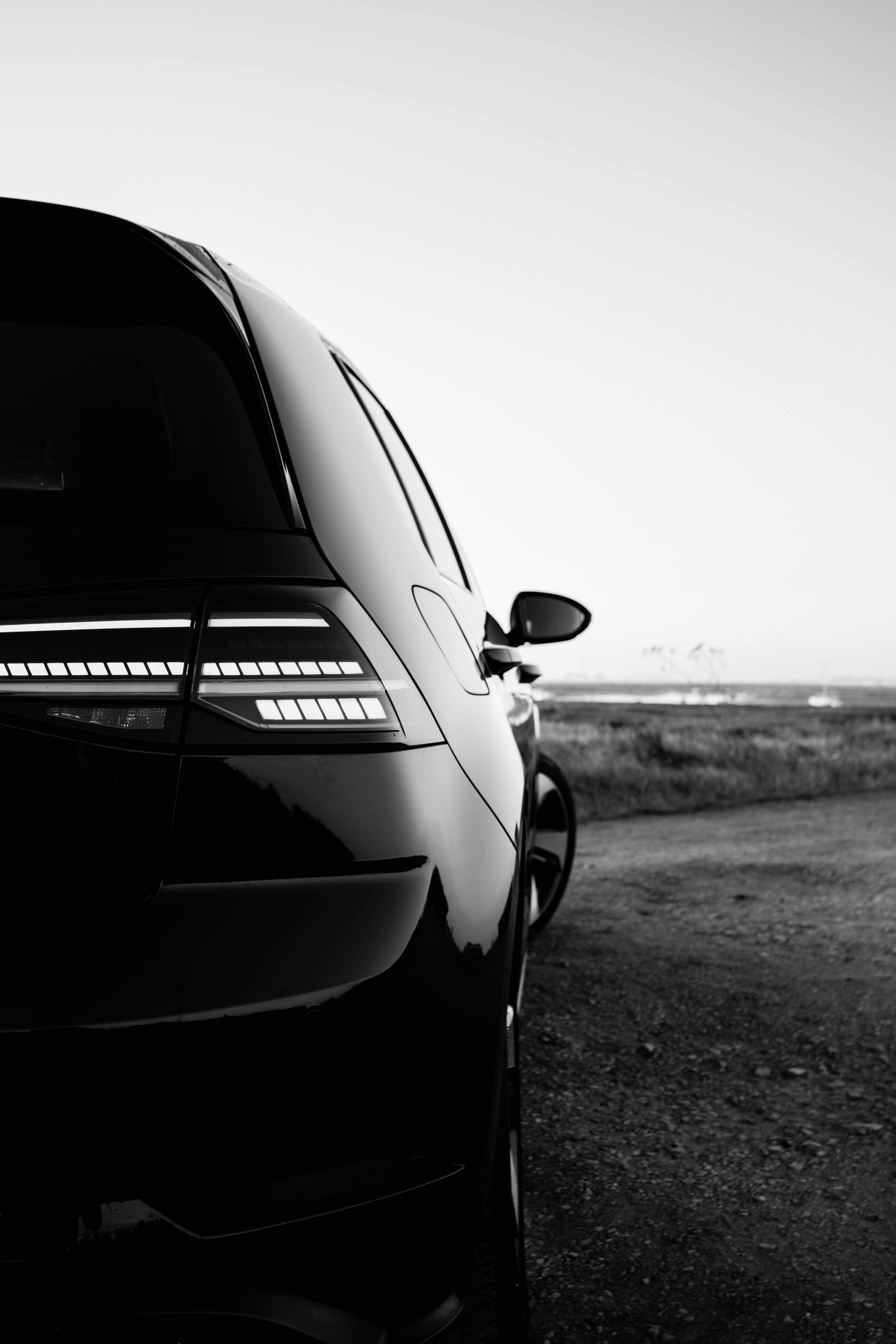黑色Volkswagen Golf GTI MK7R 酷炫風 壁紙 — 一輛時尚黑色汽車的尾燈在黃昏時分的極簡黑白路邊場景中閃耀。