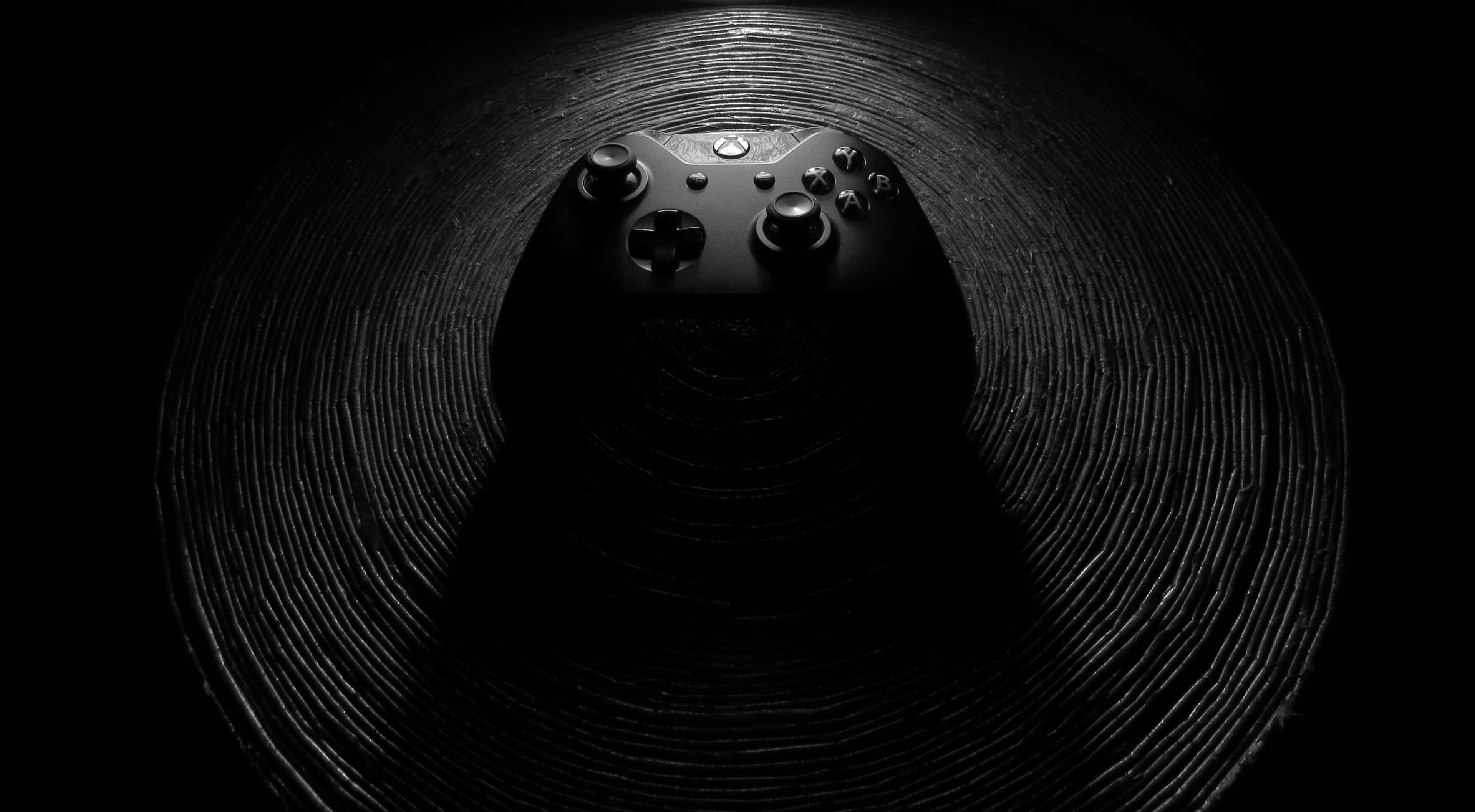 4K Gaming Consoles 桌布 壁紙 — 黑色Xbox手把置於同心脊狀暗隧道的中央，在戲劇性聚光燈下。
