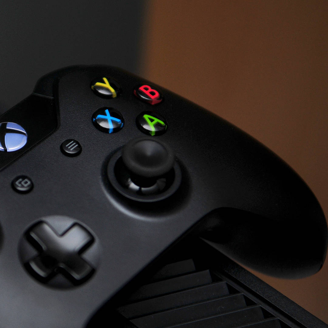 Xbox 桌布 壁紙 — 黑色Xbox手掣特寫，帶有發光彩色按鈕，背景為溫暖的棕色。