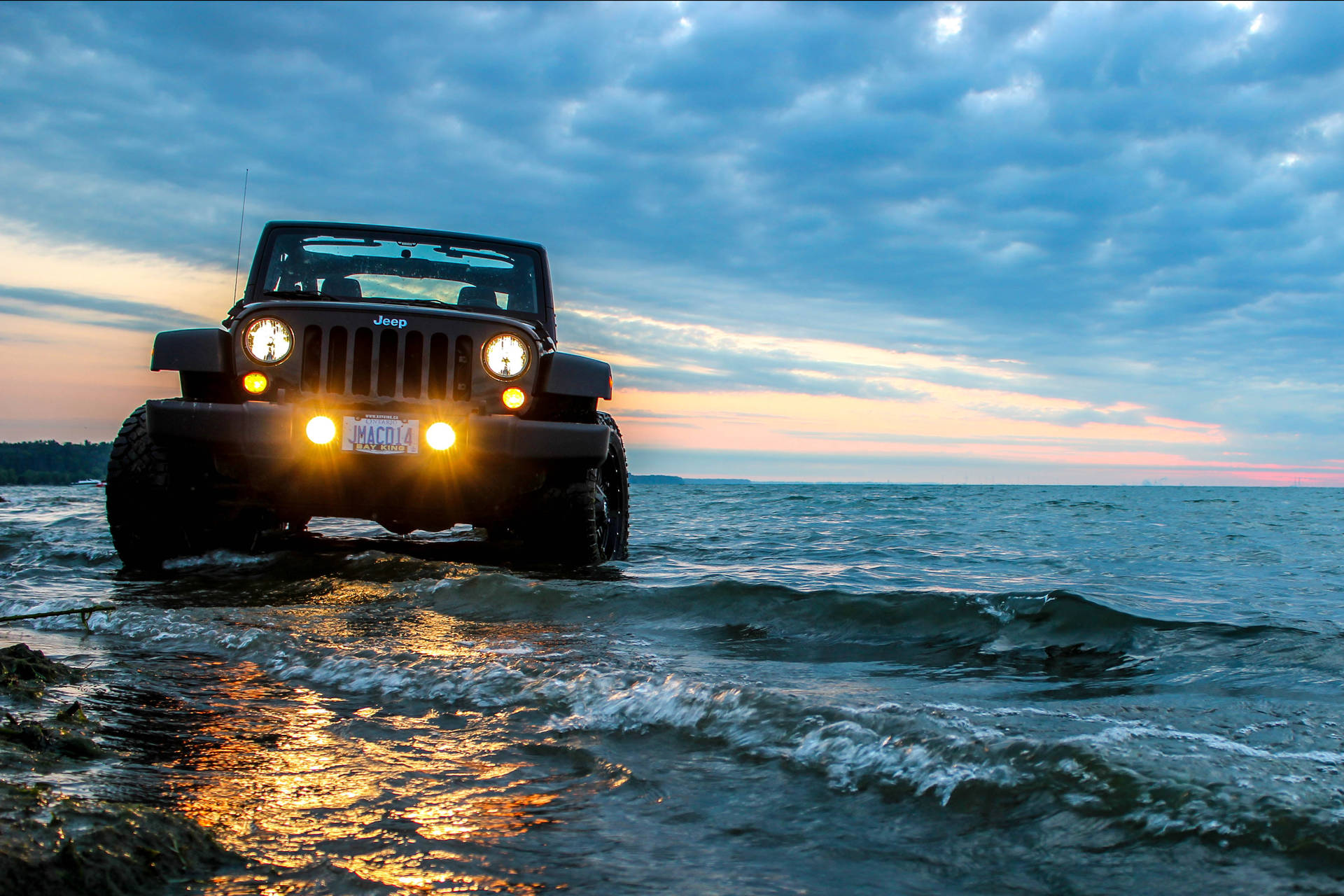 黑色Jeep在日落時分開著車頭燈行駛在海水中。