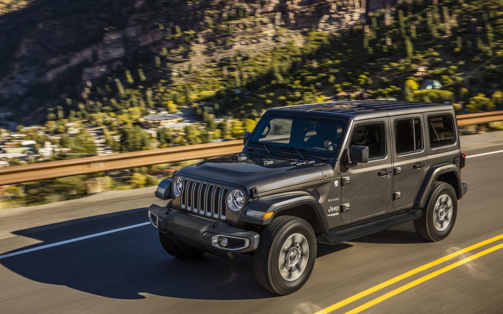 黑色Jeep Wrangler在山路上行駛，背景有森林和峭壁