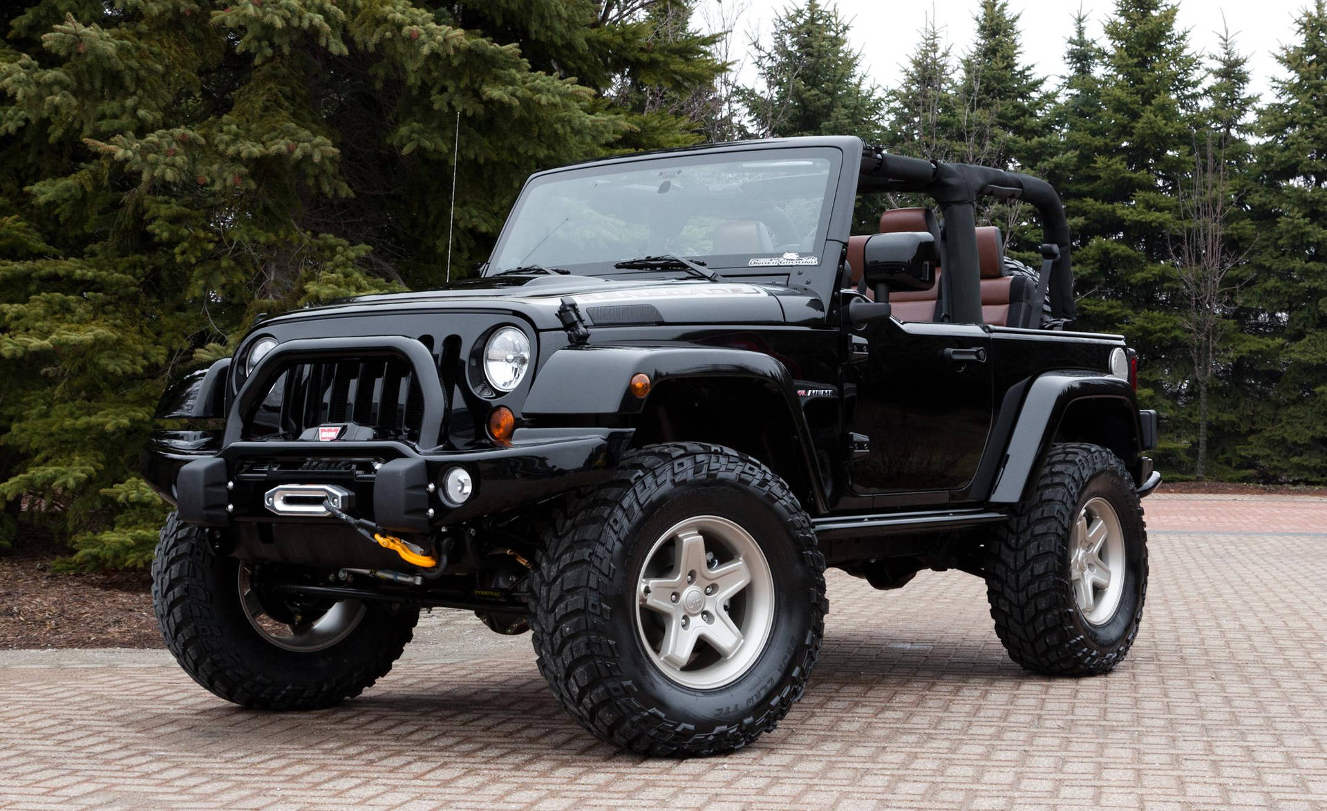 黑色Jeep Wrangler停在磚砌車道上，後面有常青樹