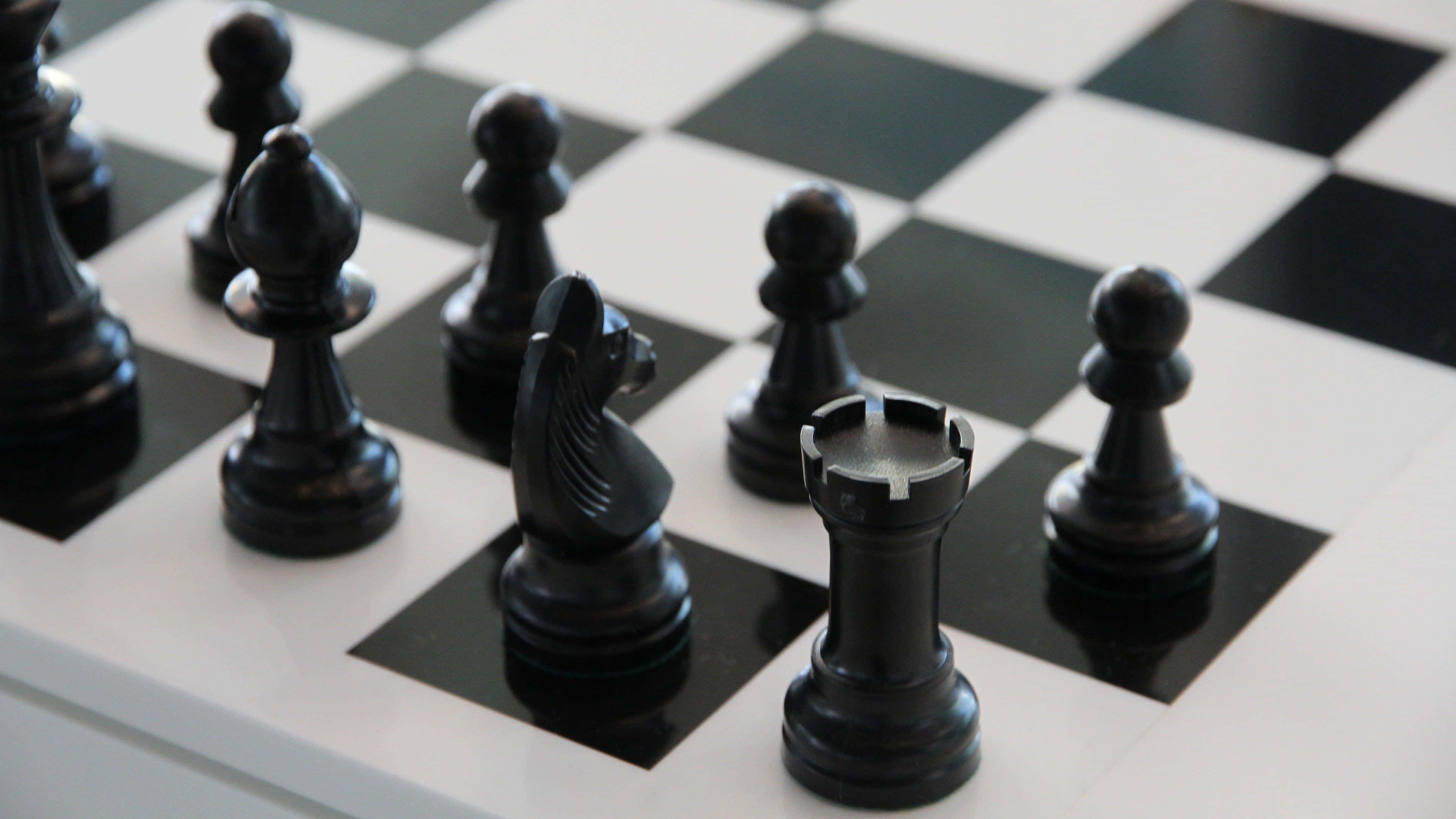 國際象棋 桌布 壁紙 — 黑色國際象棋棋子喺棋盤上嘅特寫，光線柔和，景深較淺。