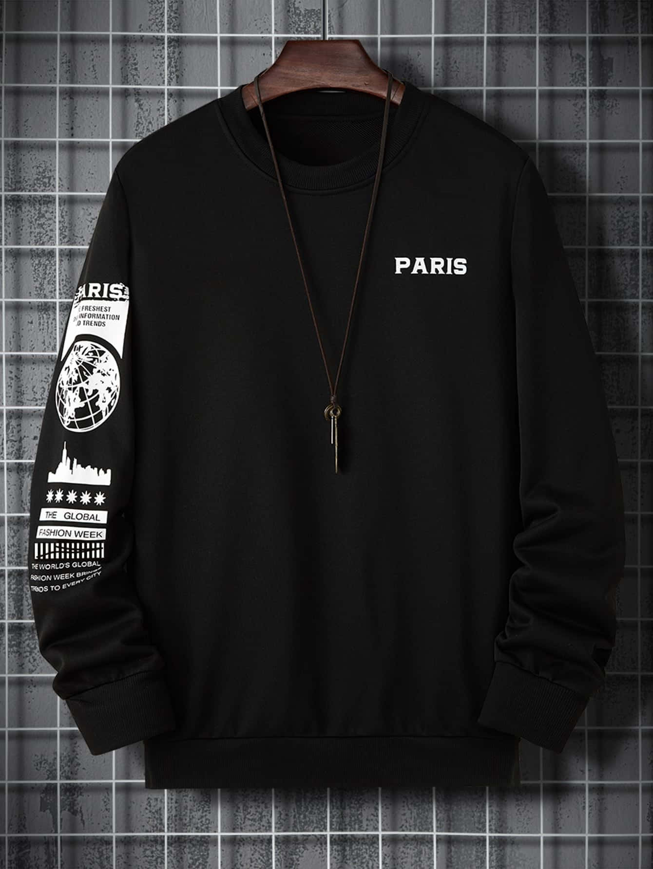 Black Clothing 桌布 壁紙 — 黑色圓領運動衫，帶有白色 'PARIS' 文字和圖案袖子，掛在木衣架上，背景是灰色瓷磚牆。