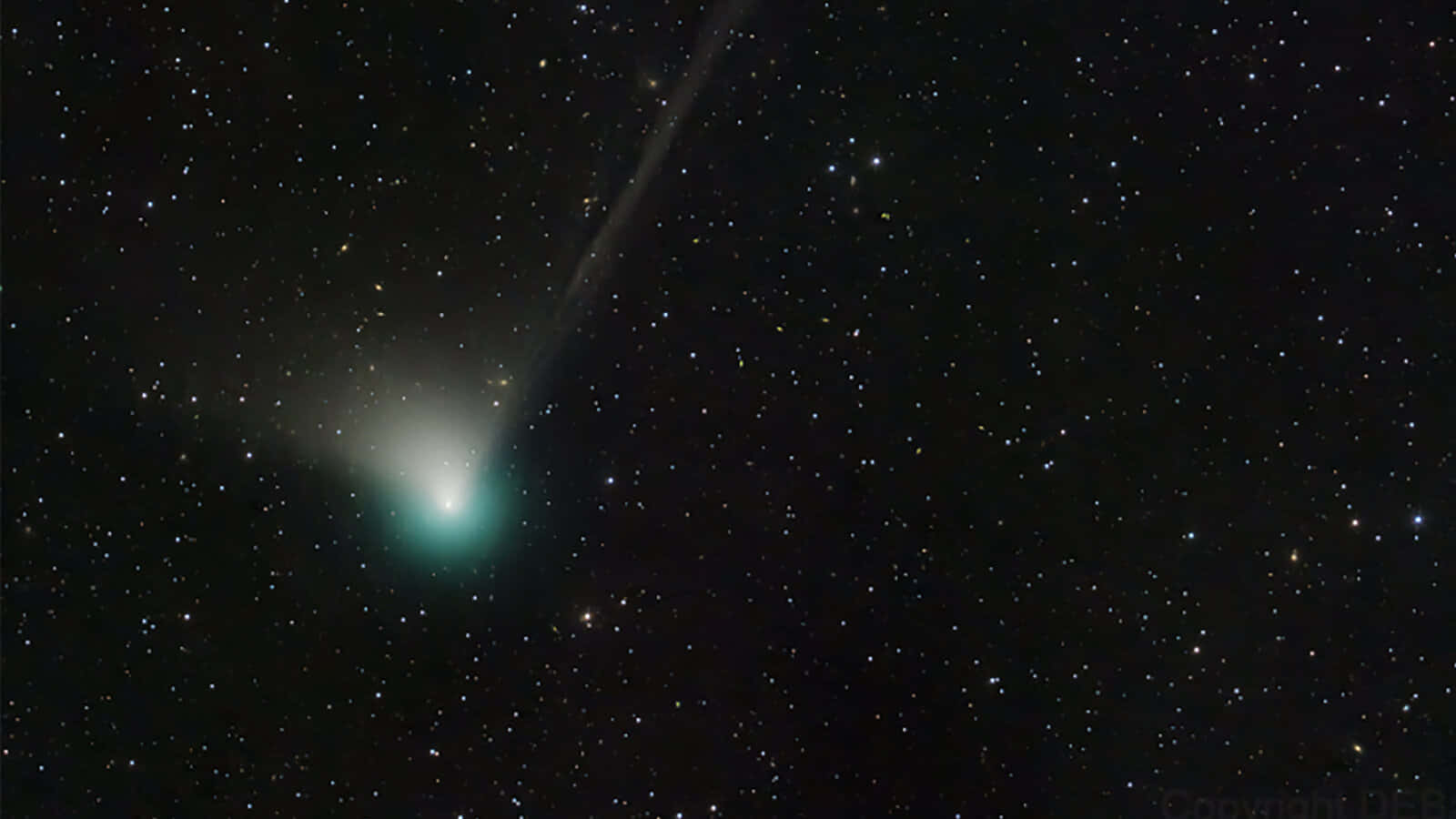 一顆帶有明亮尾巴的綠色彗星在夜空中無數星星之間閃耀。