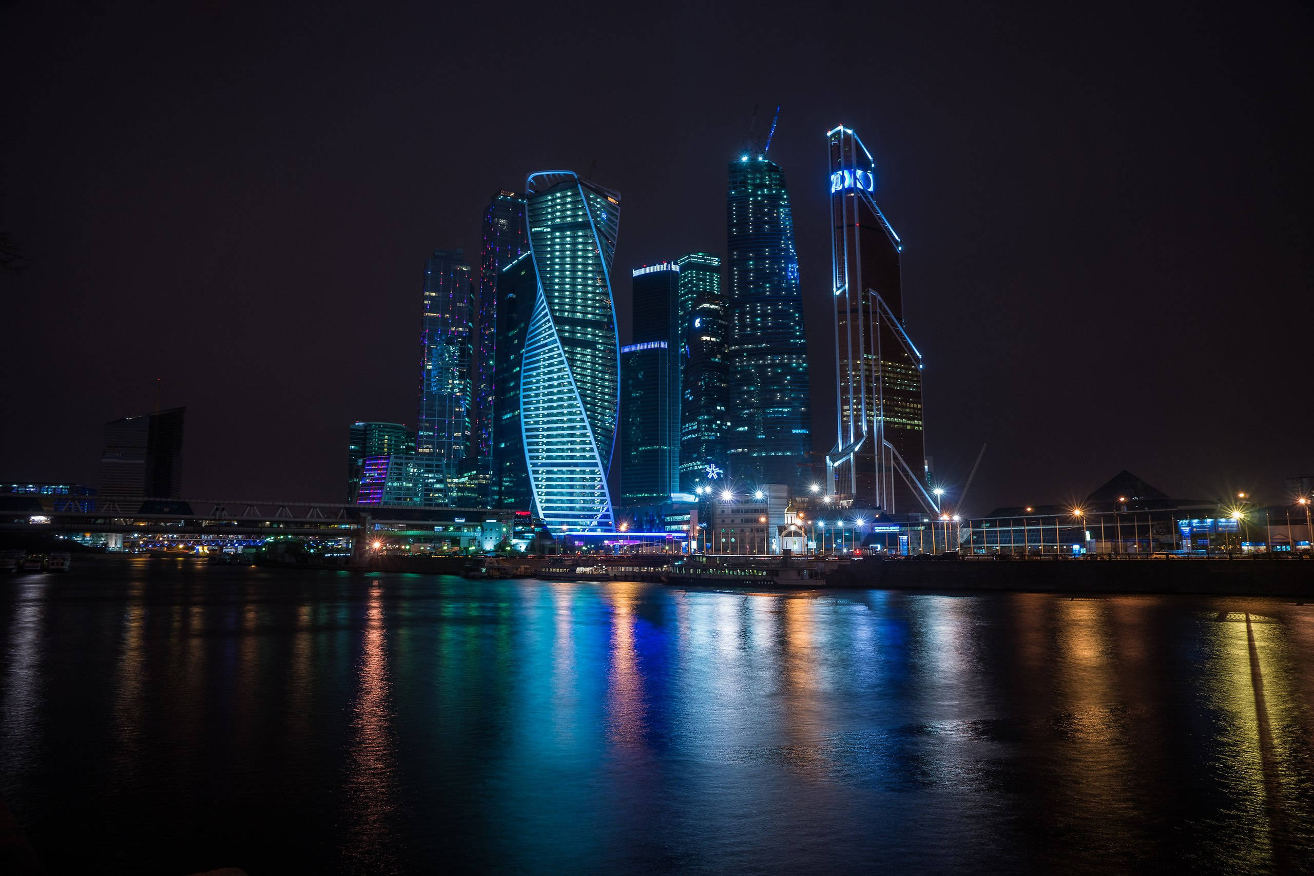 Russia 桌布 壁紙 — 黑色天空下，發光的摩天大樓倒映在黑暗水面上嘅夜景。