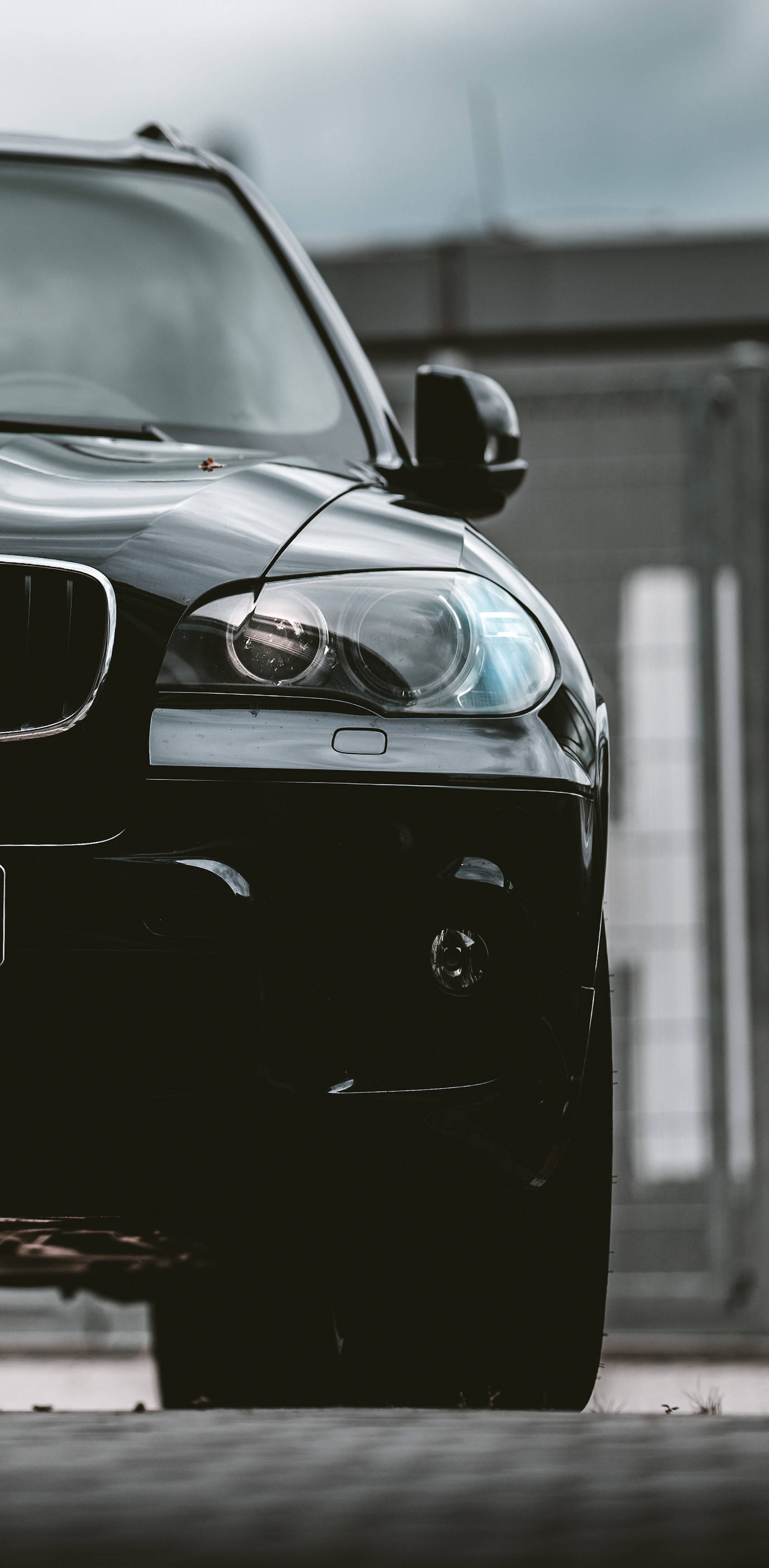 黑色寶馬手機專用壁紙 壁紙 — 一架時尚的黑色BMW SUV在陰天之下，以其光澤表面和銳利車頭燈主導畫面。