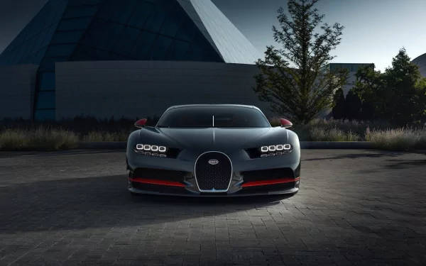 一輛帶有紅色點綴的灰色Bugatti超級跑車在黃昏時停泊在現代建築前。