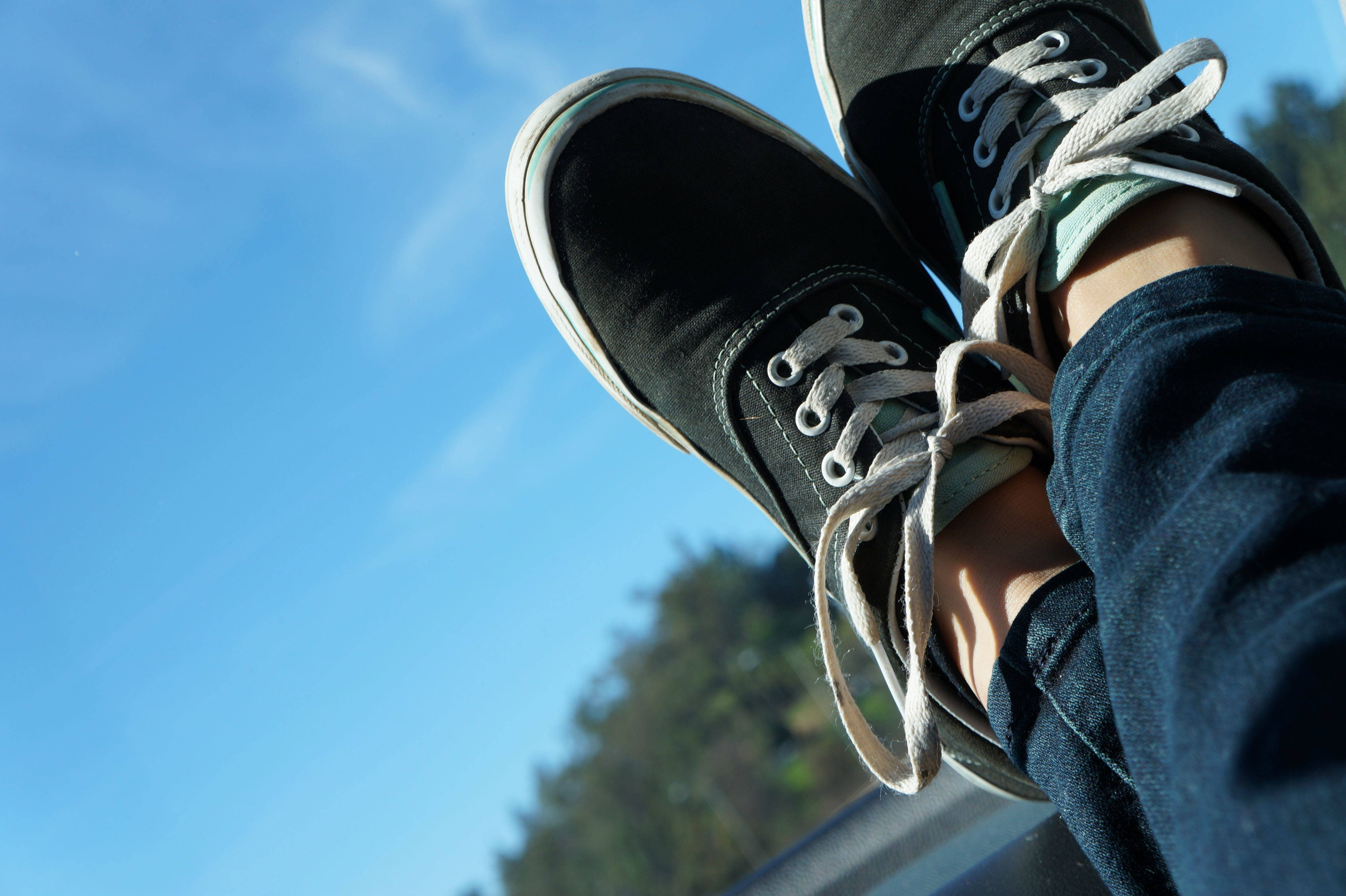 Vans 桌布 壁紙 — 黑色帆布運動鞋配白色鞋帶，隨意地靠在清澈的藍天和遠處的綠樹旁。