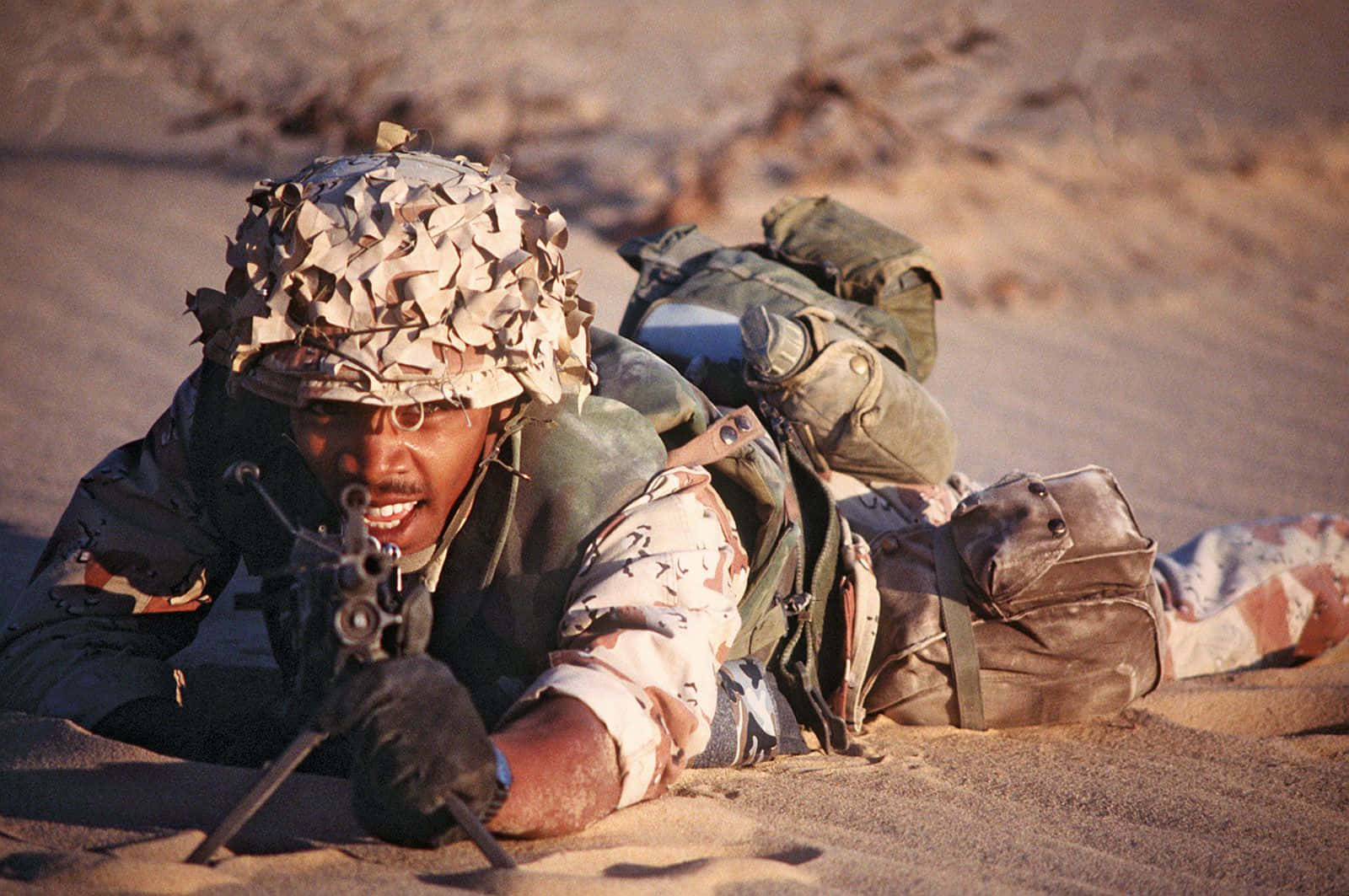 沙漠裝備的士兵在沙地中持步槍爬行。
