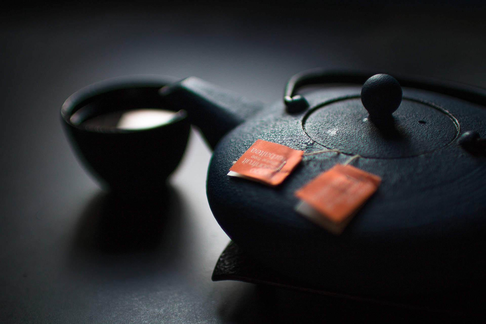 深色茶壺和杯子，帶橙色茶包，置於陰影表面。