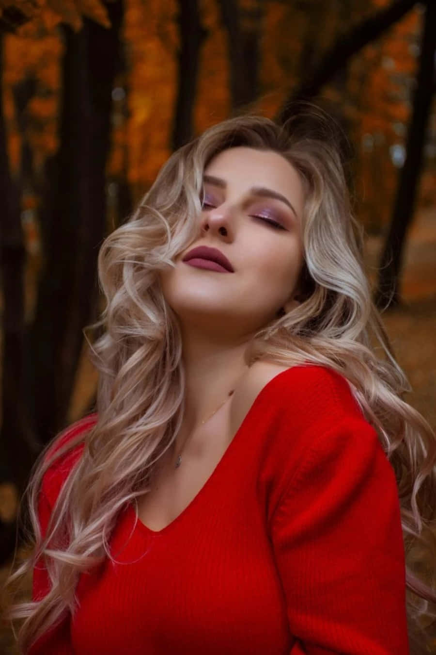 穿著紅色毛衣的女性在秋日森林中閉上眼睛。