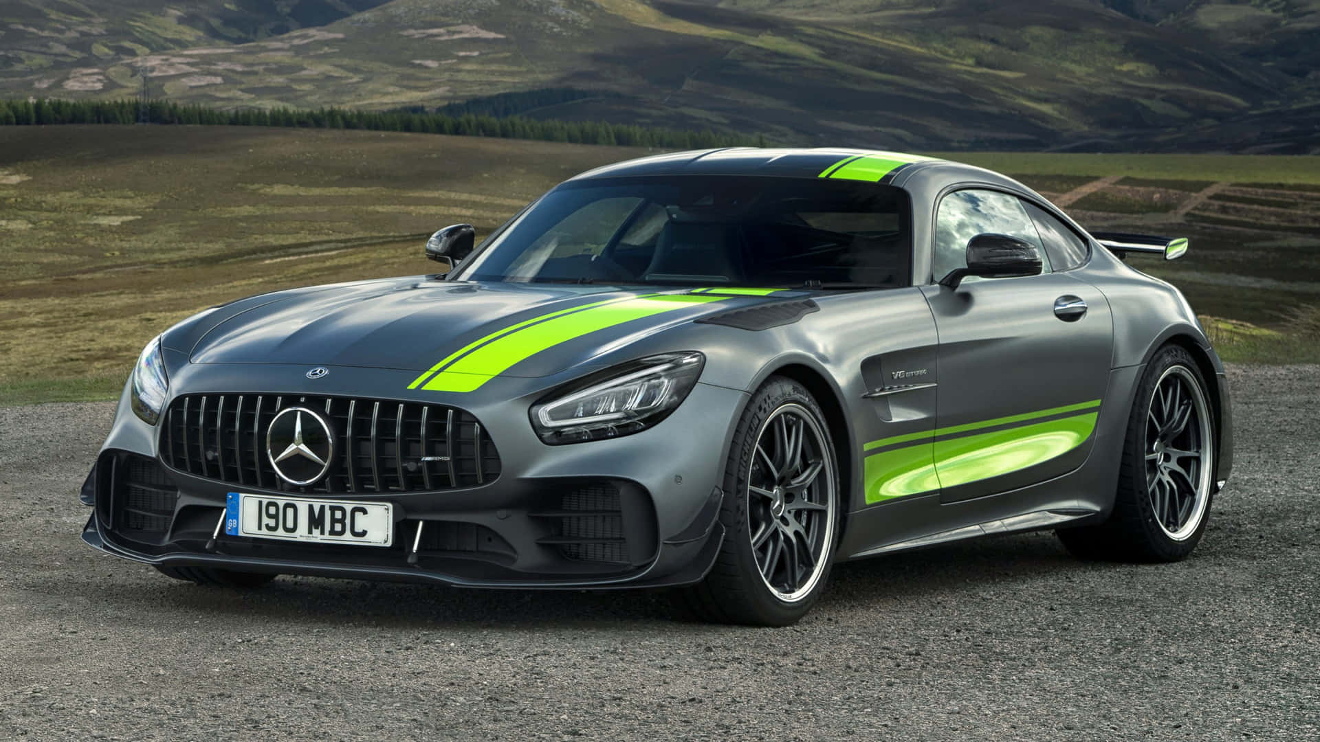 黑色梅賽德斯-奔馳AMG GT R Pro風景背景 壁紙 — 一架流線型灰色Mercedes-AMG GT，帶有螢光綠色賽車條紋，停泊在碎石地上，背景是連綿起伏的山丘。