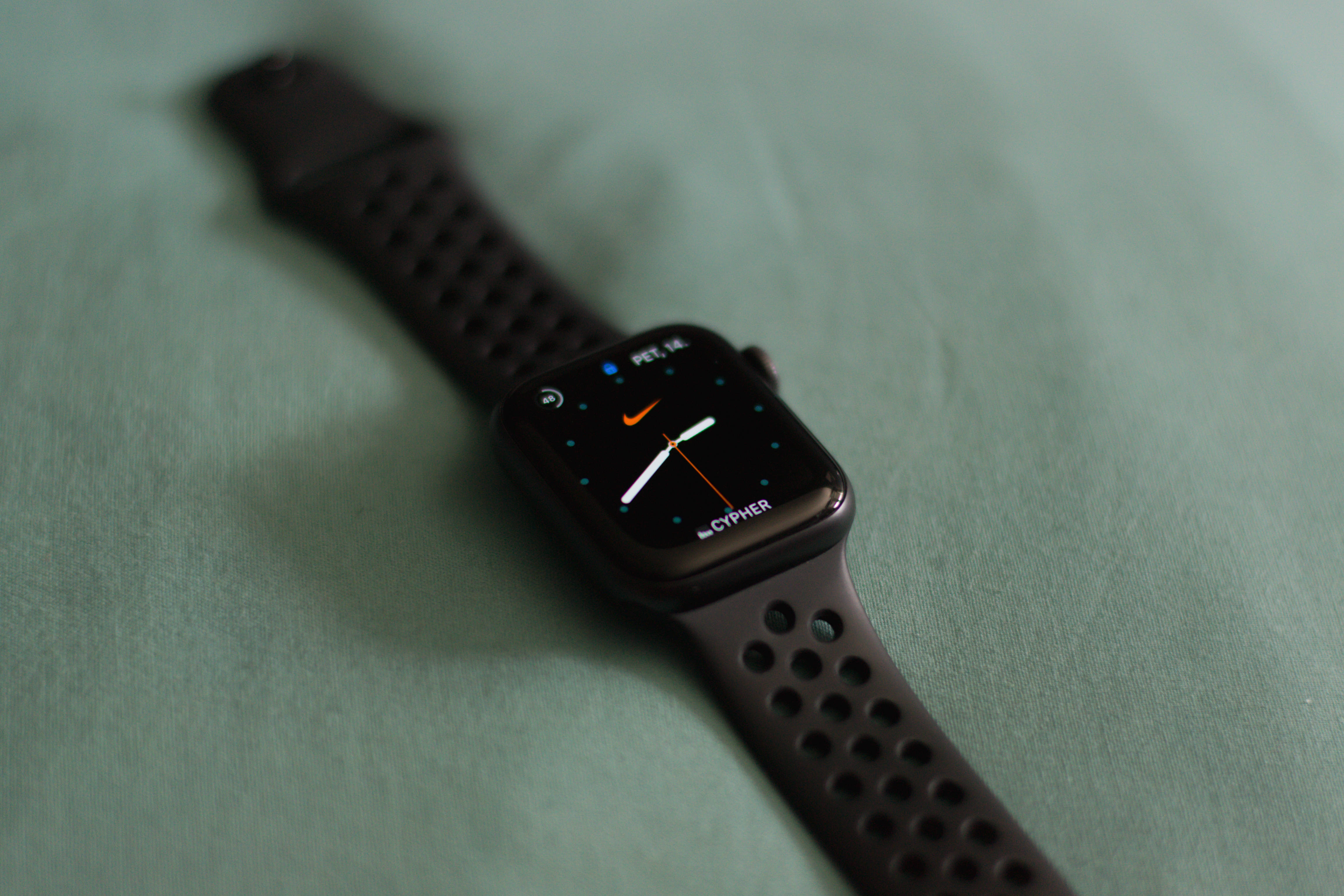 黑色極簡智能手錶 壁紙 — 一隻黑色Apple Watch配Nike錶面，放在柔軟的綠色布料表面上。