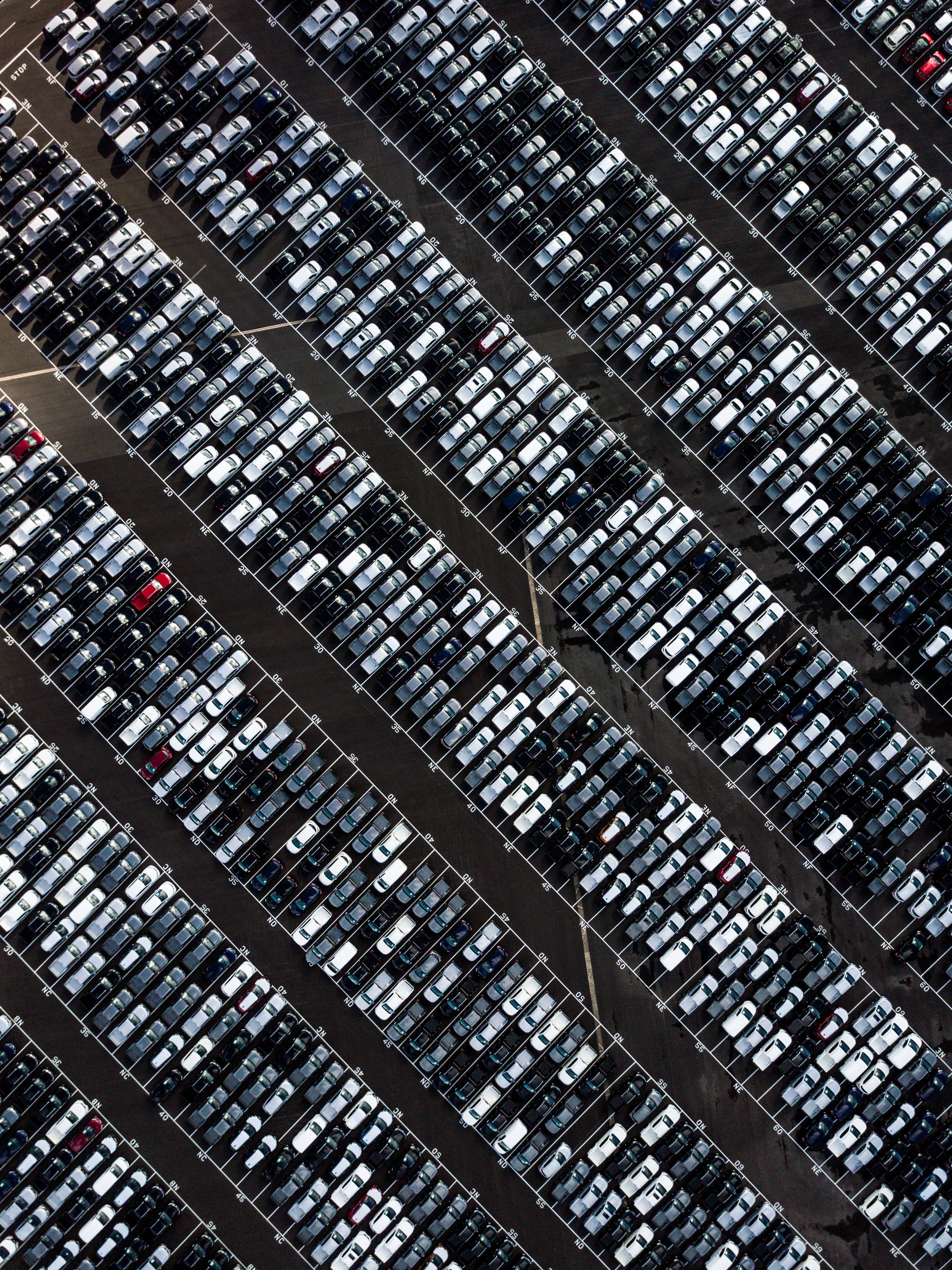 黑色機器人停車場 壁紙 — 廣闊停車場的鳥瞰圖，整齊排列的汽車行列，主要是白色和黑色，帶有少量紅色點綴。