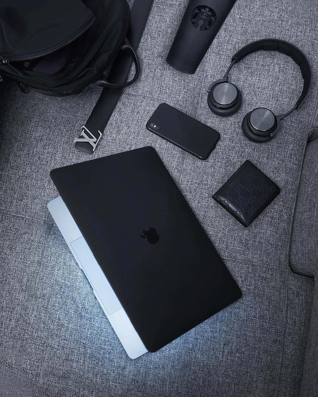 黑色的神秘魅力 壁紙 — 一部時尚的黑色手提電腦放在灰色紋理表面上，周圍環繞著現代科技配件和奢侈品。