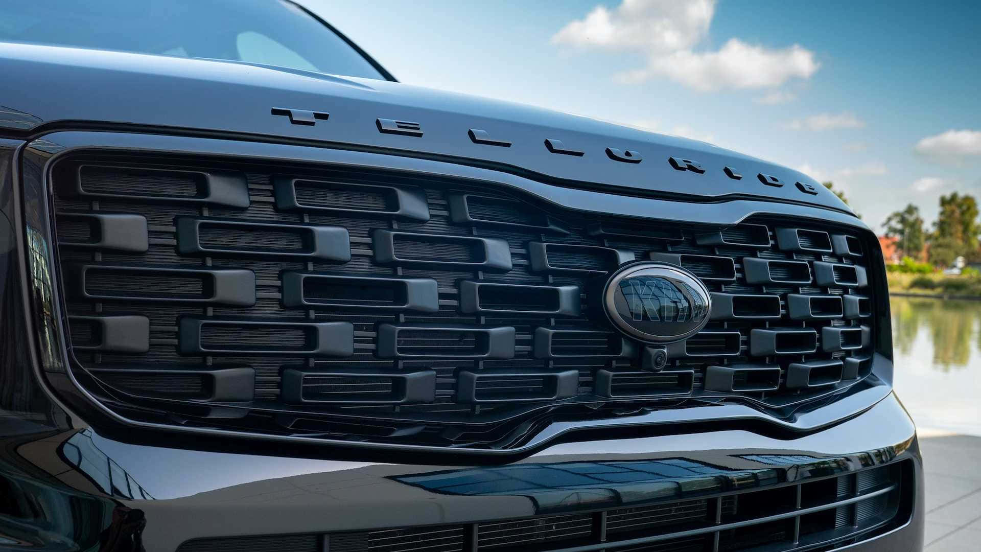 Kia Telluride 桌布 壁紙 — 黑色福特 Taurus 鬼面罩近鏡，帶有鍍鉻飾邊，反射出明亮的藍天和水面。