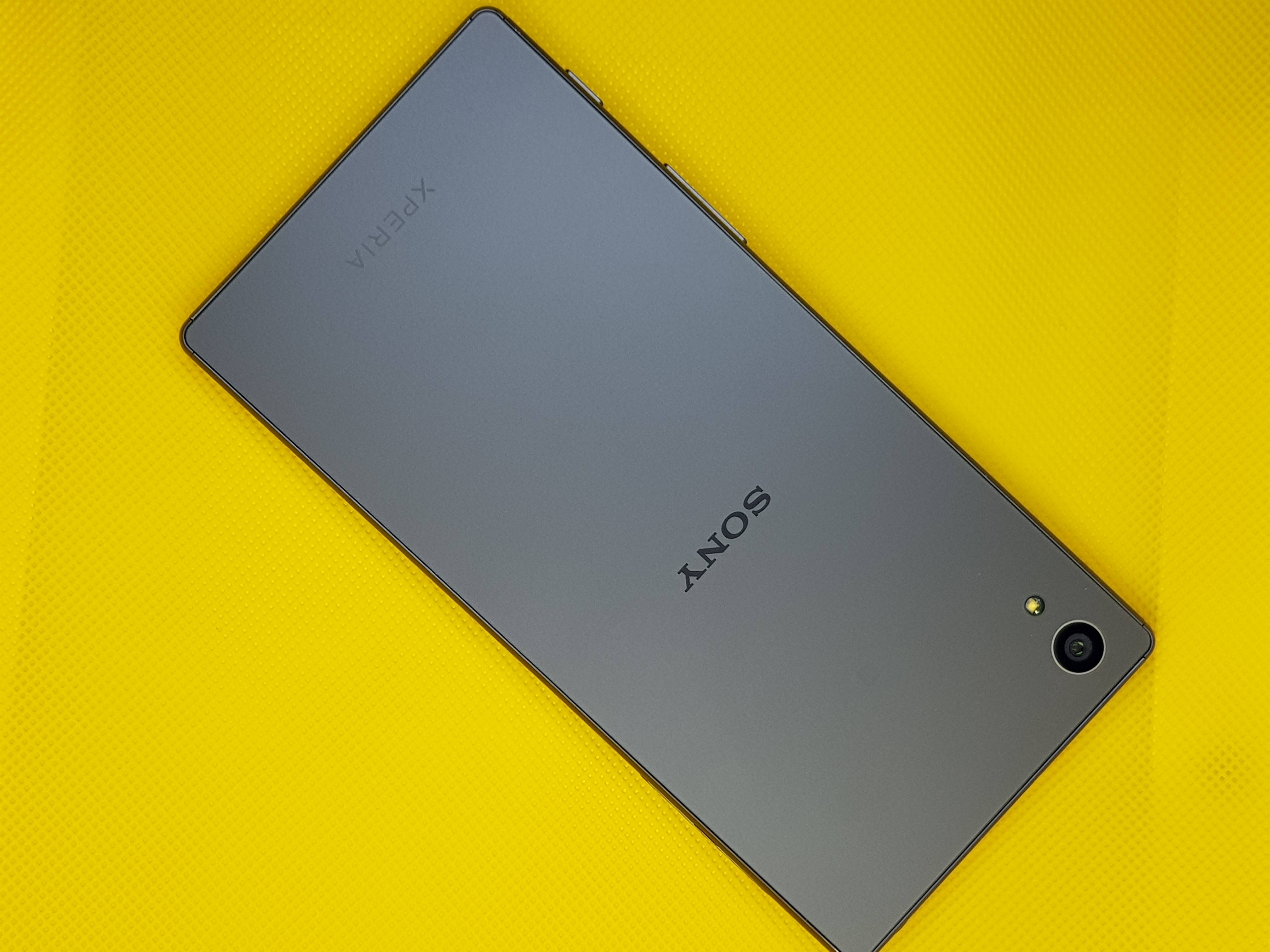 黑色索尼Xperia手機 壁紙 — 一部時尚的灰色Sony Xperia智能手機對角放置在充滿活力的黃色紋理表面上。