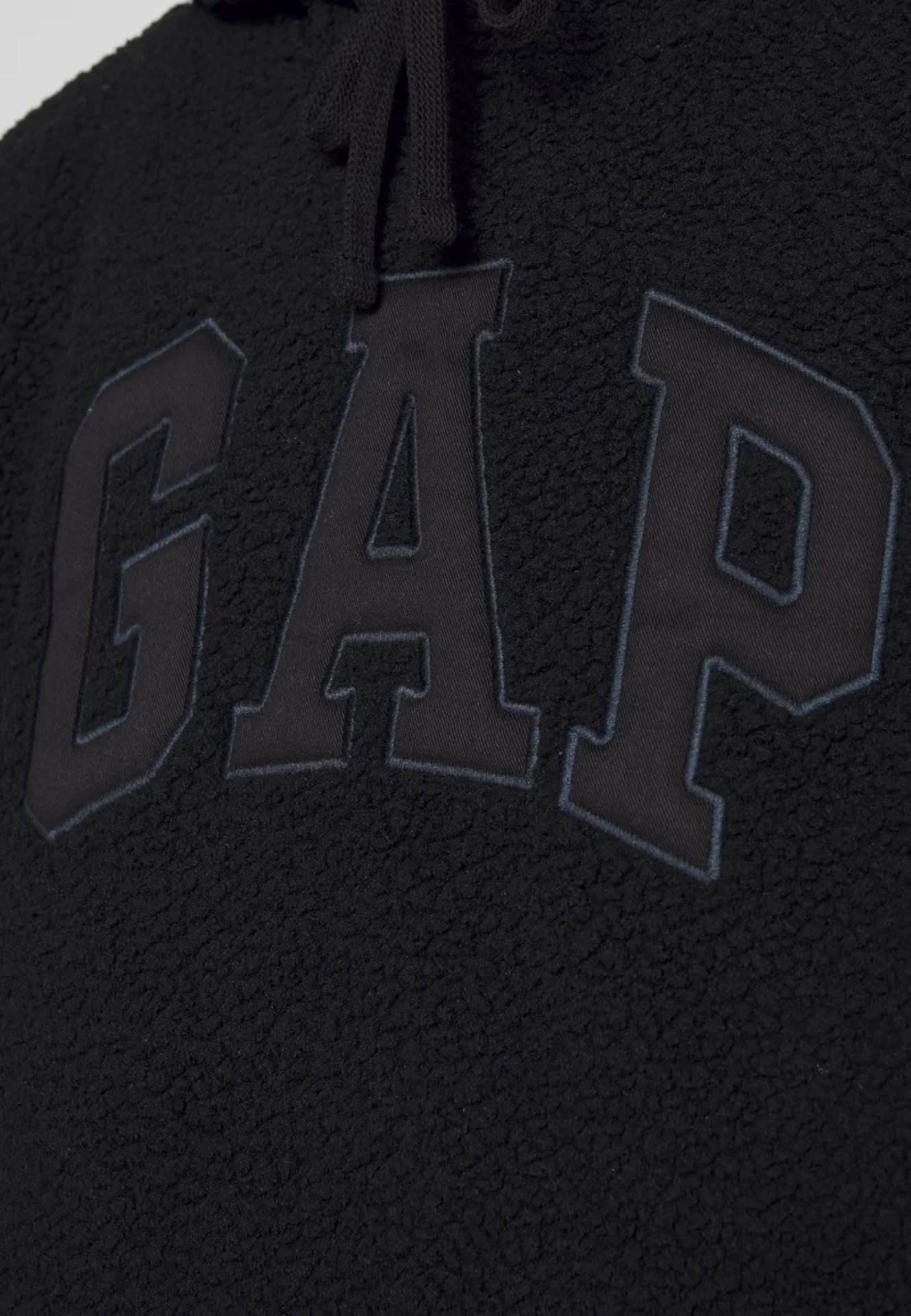 黑色絨毛上繡製Gap標誌 壁紙 — 黑色抓絨連帽衫特寫，帶有粗體刺繡GAP標誌和抽繩。