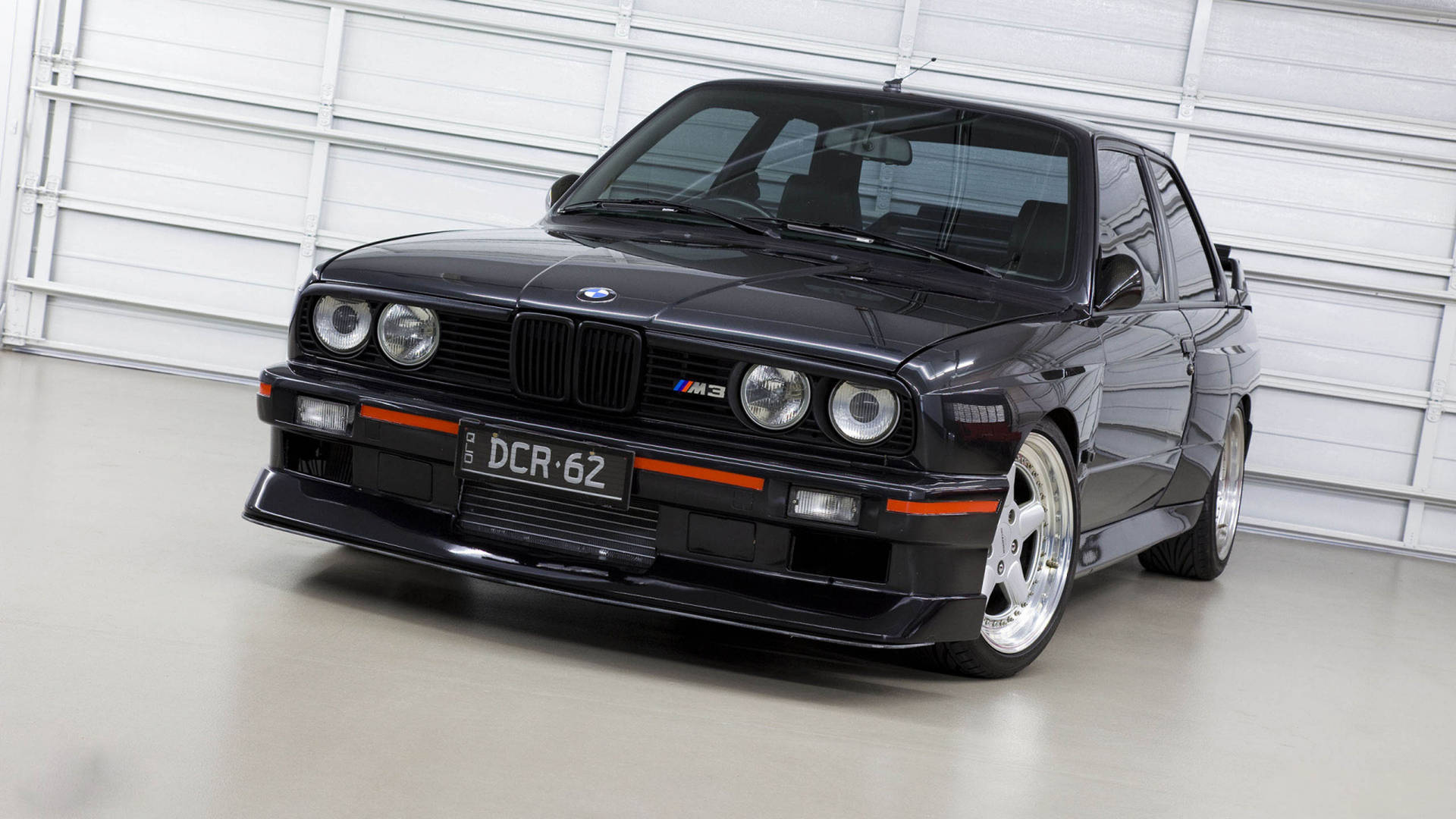 黑色BMW M3跑車帶橙色飾邊停在白色車庫中。